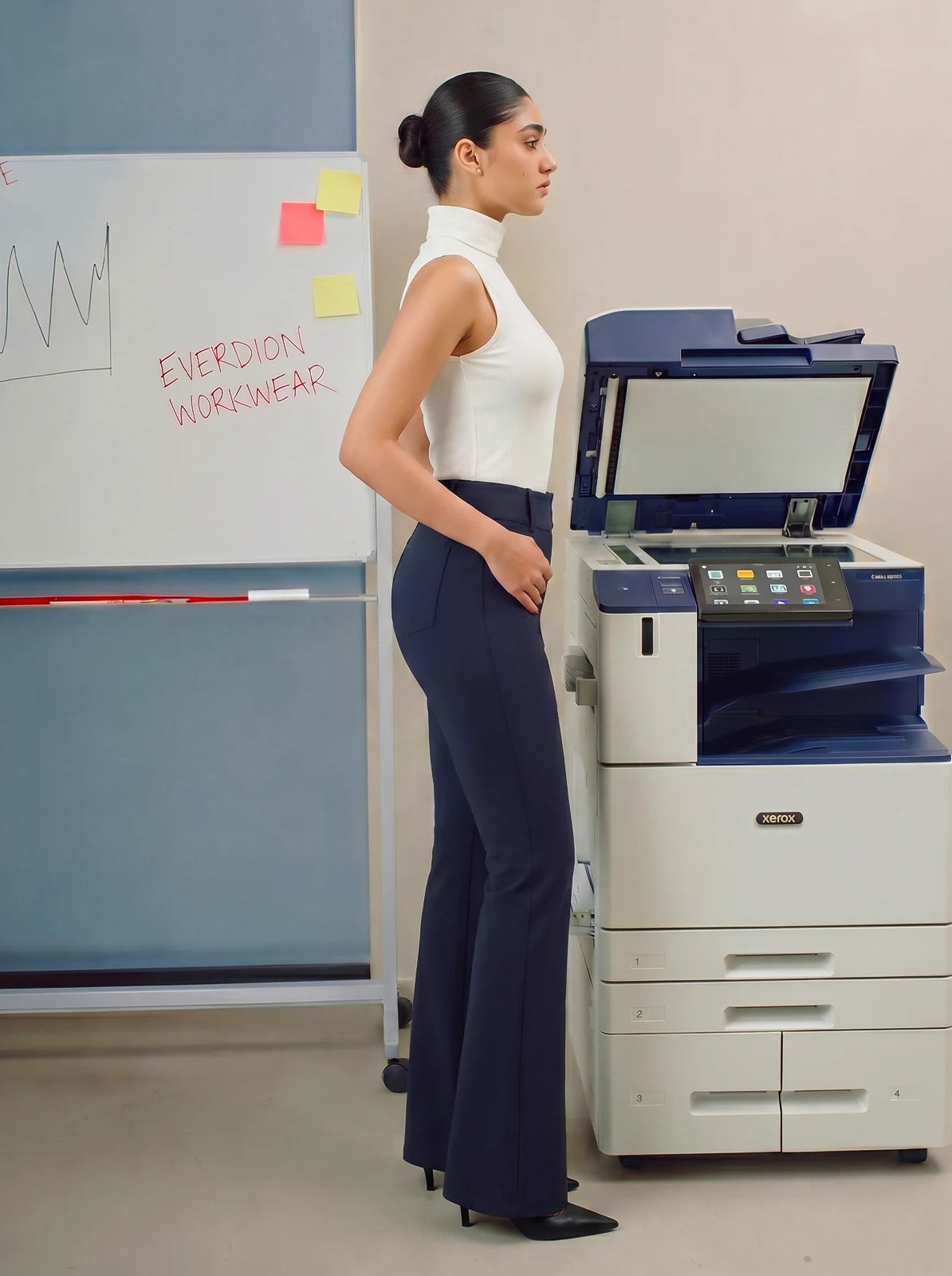 Person wearing navy blue pants standing in an office setting with a printer in the background.