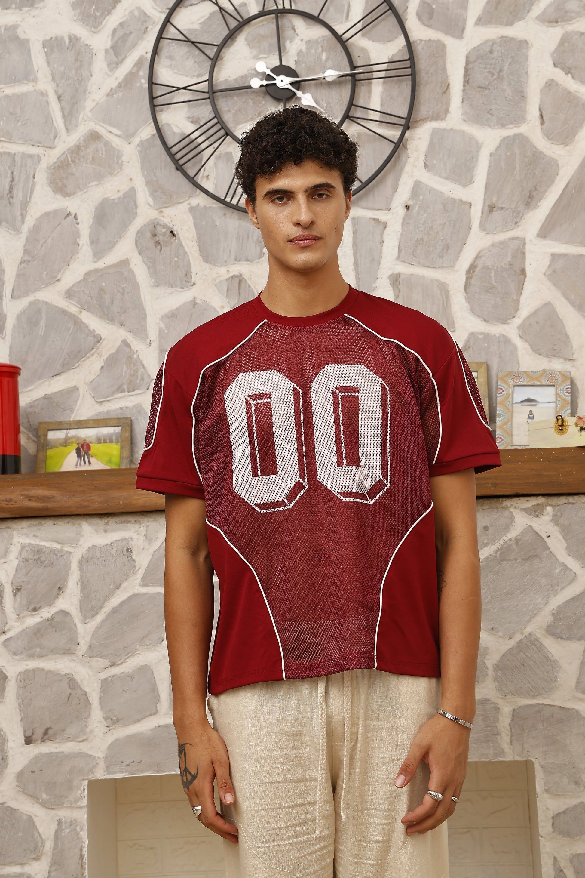 Man wearing a red sports jersey with white lettering against a stone wall.