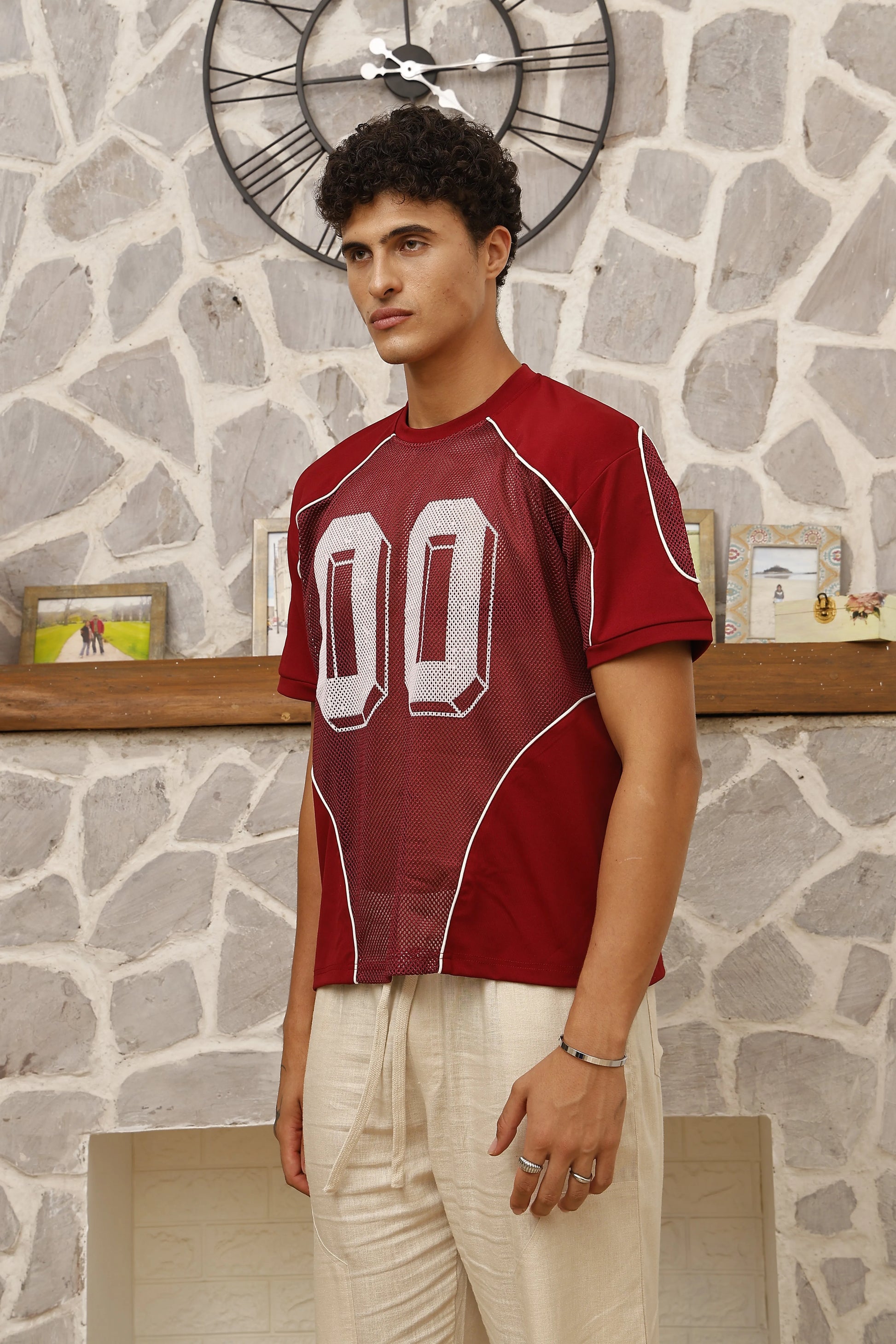 Man wearing a red sports jersey with white lettering against a stone wall.