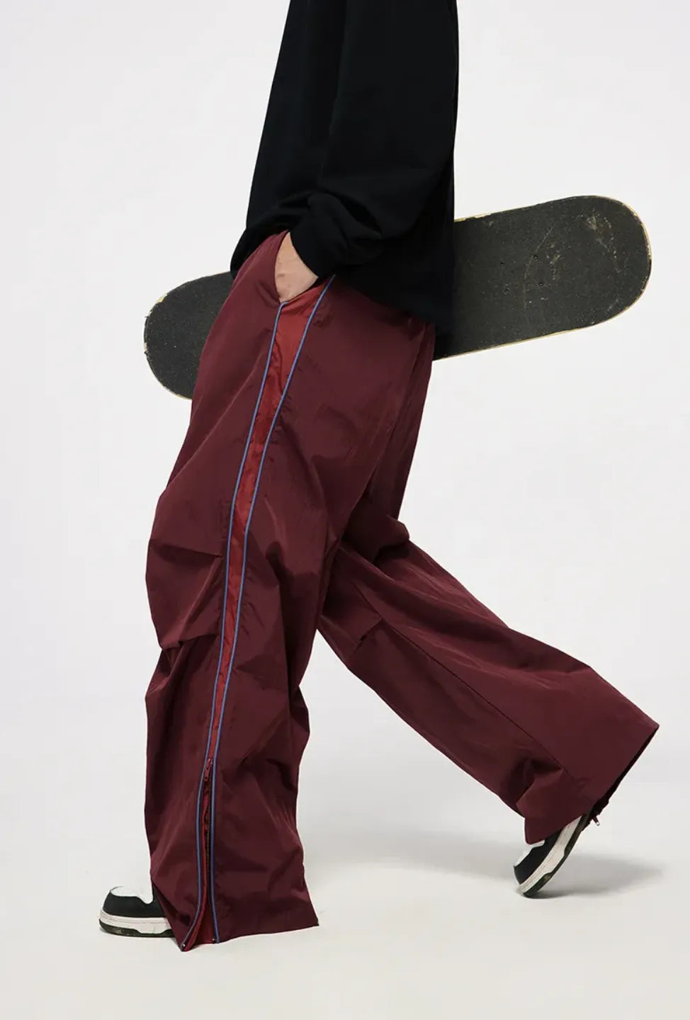 Person wearing maroon pants with a black skateboard on a white background