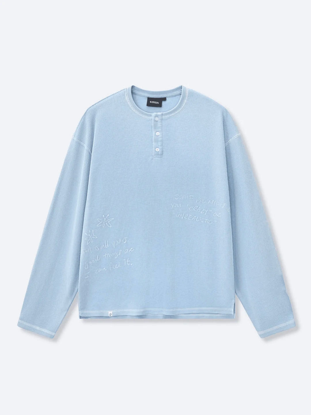 A light blue long-sleeve henley t-shirt with tonal embroidered text on the front