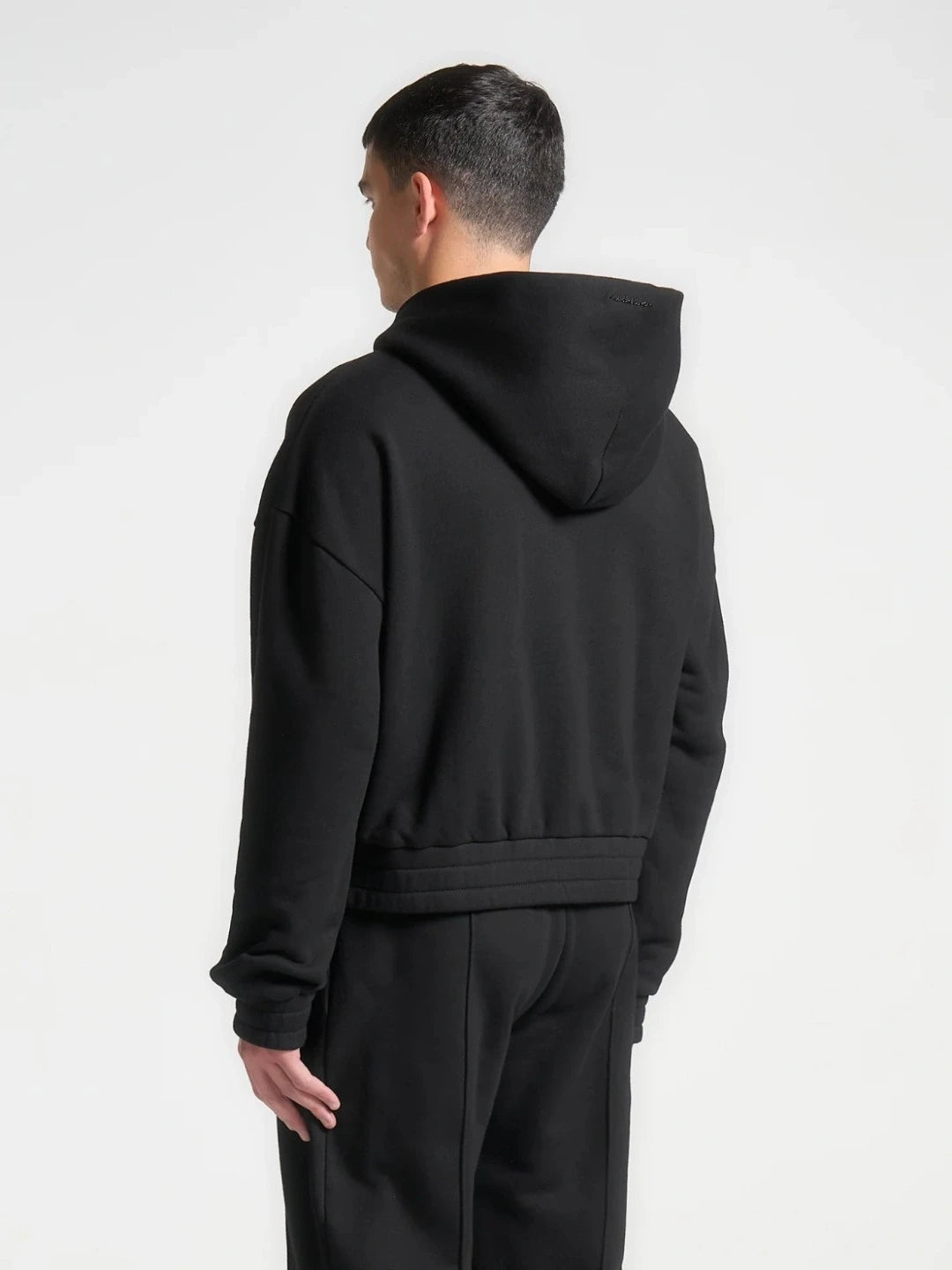 Person wearing a black hoodie and pants on a white background