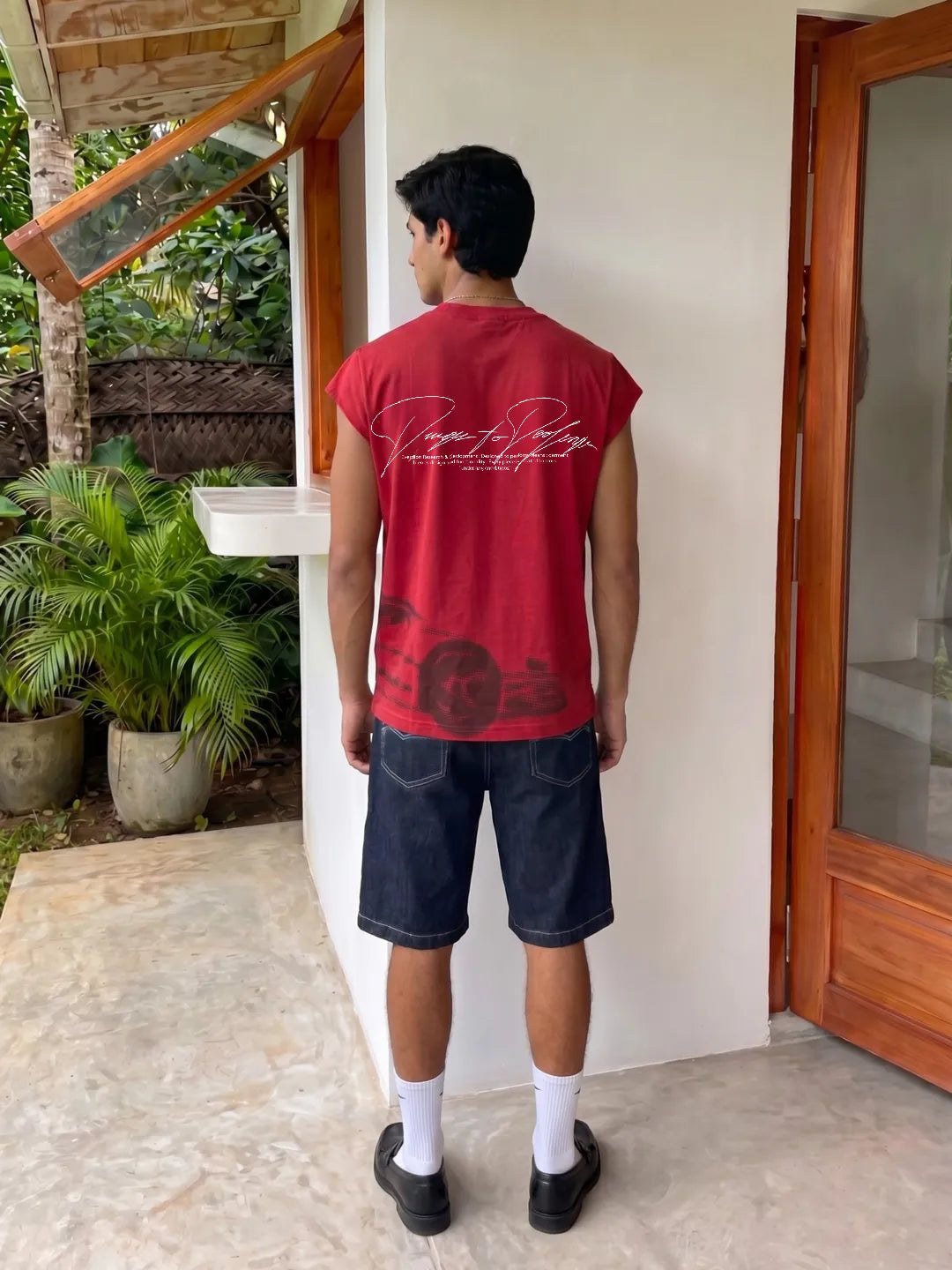Person wearing a red Oversized Tank Top with text and dark shorts standing in front of a house entrance.
