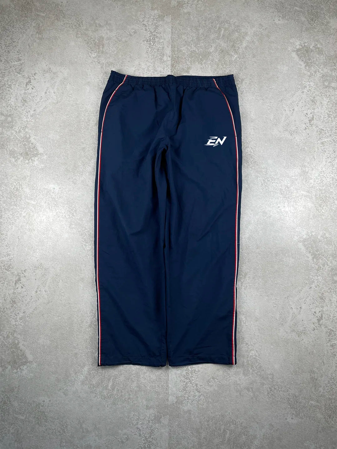 Navy blue athletic pants with a logo on a grey concrete surface