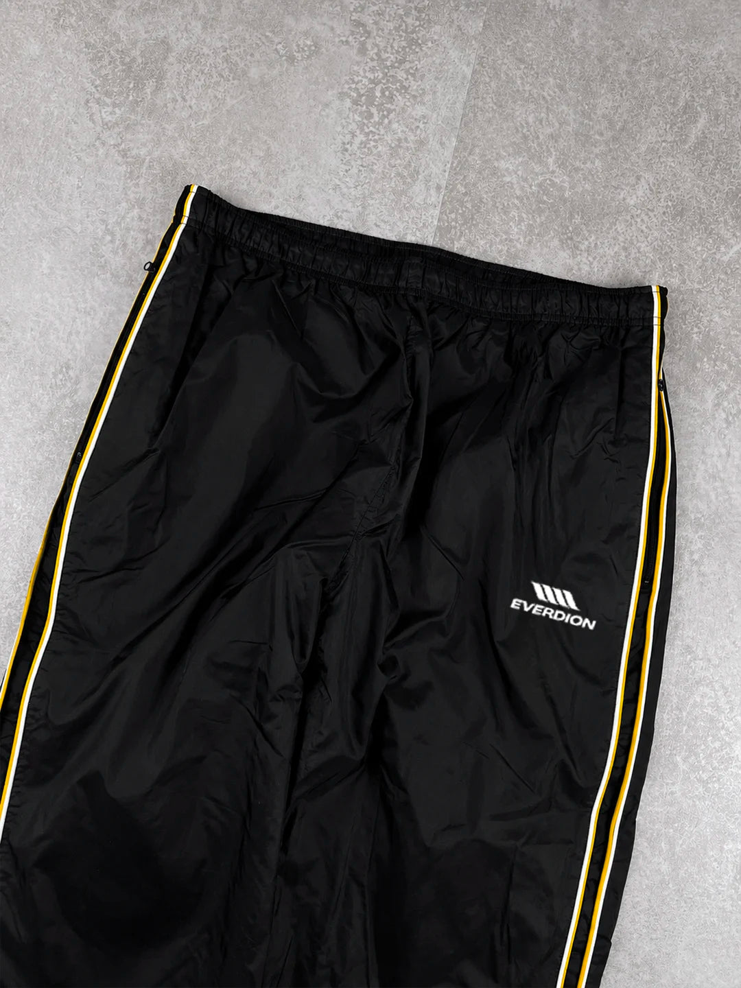 Black track pants with a red stripe and brand logo on a grey background
