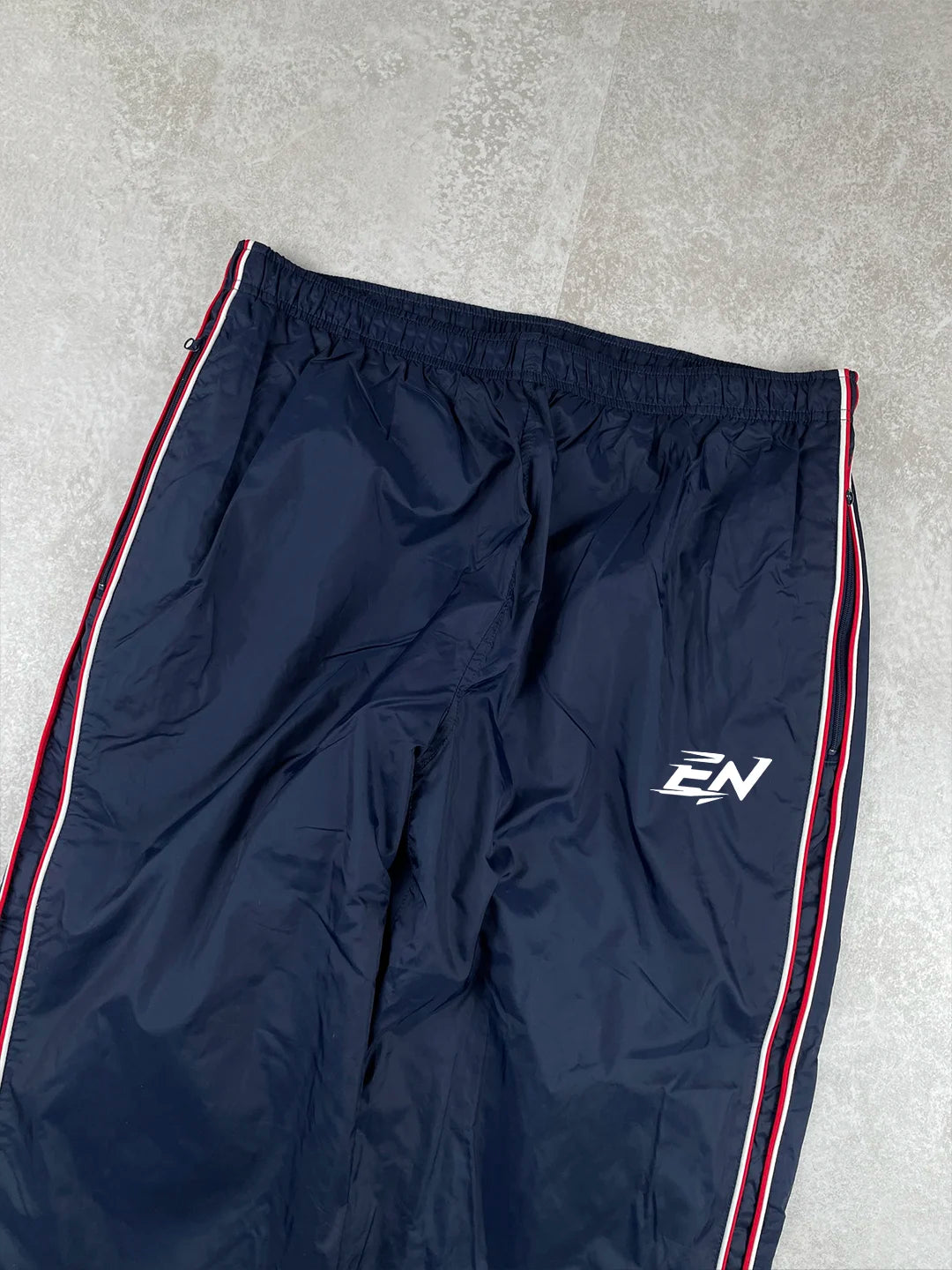 Navy blue tracksuit pants with red and white stripes on a grey surface