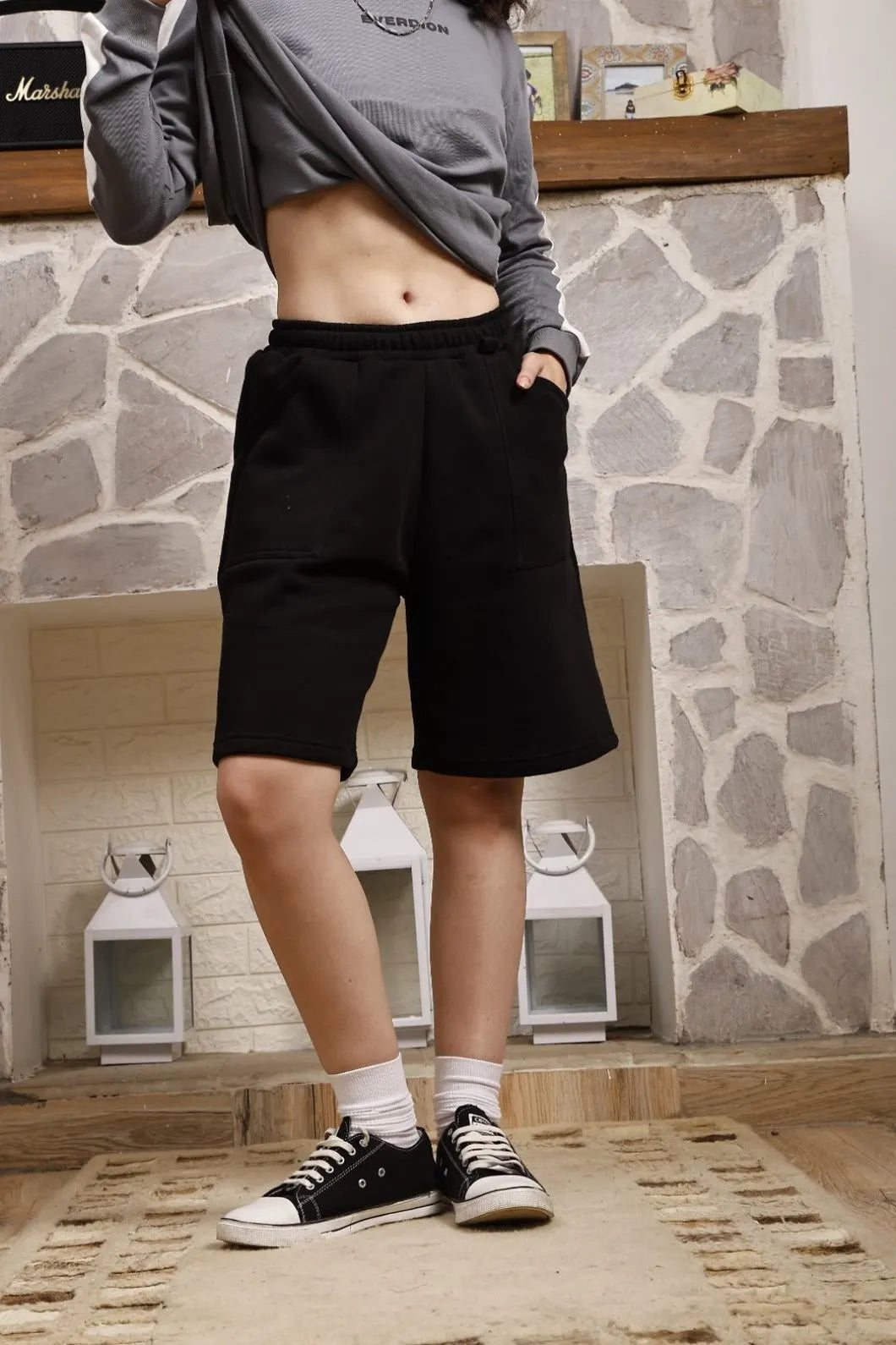 Person wearing black shorts and a gray sweatshirt in front of a stone fireplace.