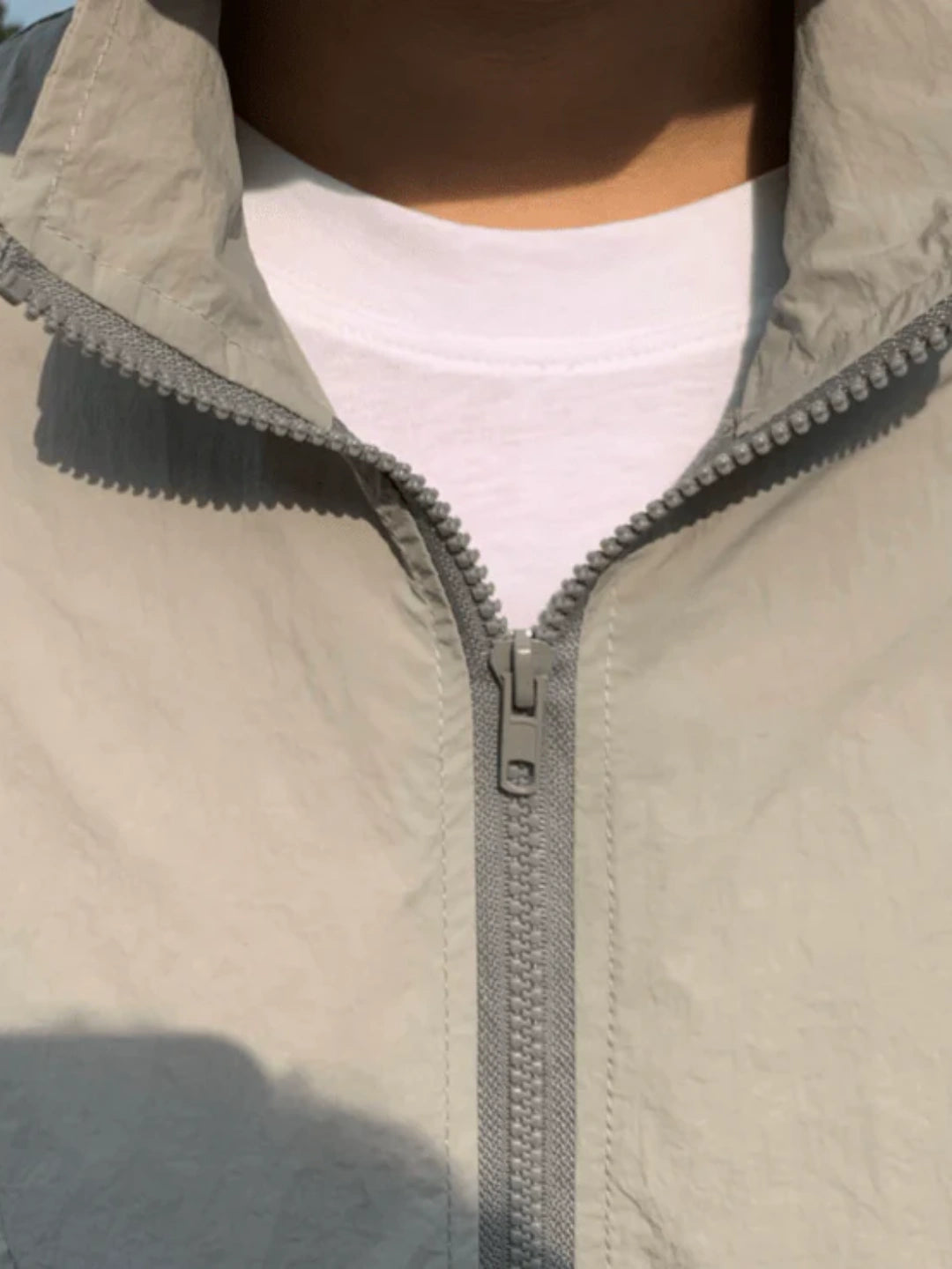 Close-up of a person wearing a beige jacket with a zipper, with a blurred background.
