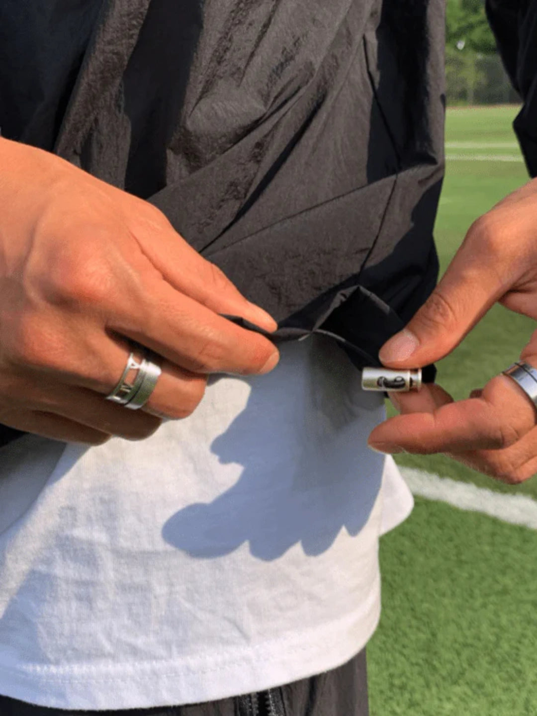 Person holding a small object near a black jacket on a grassy field