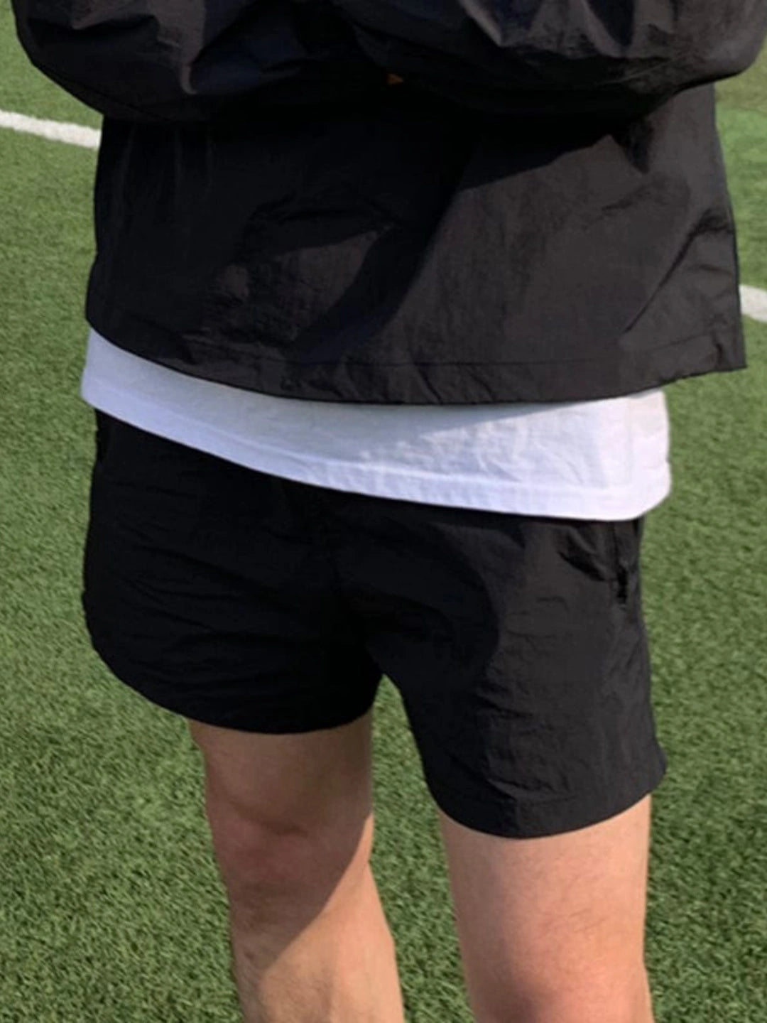 Person wearing a black jacket, white shirt, and black shorts on a grassy field.