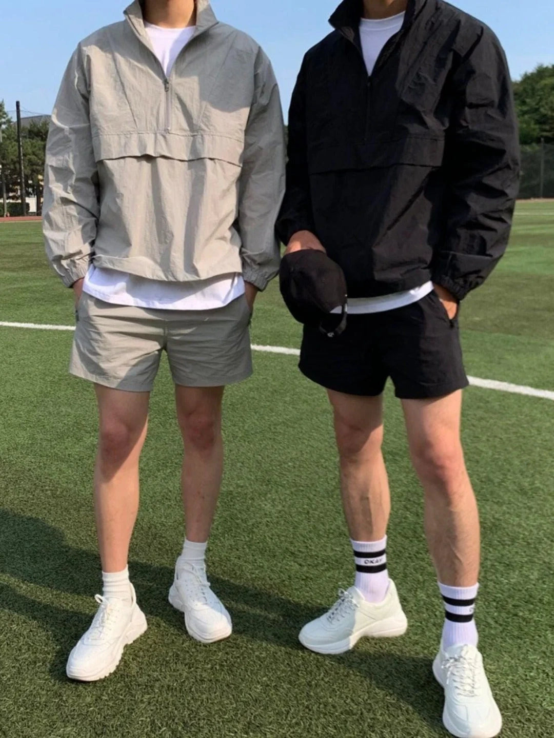 Two people wearing matching outfits with jackets, shorts, and white sneakers on a grassy field.