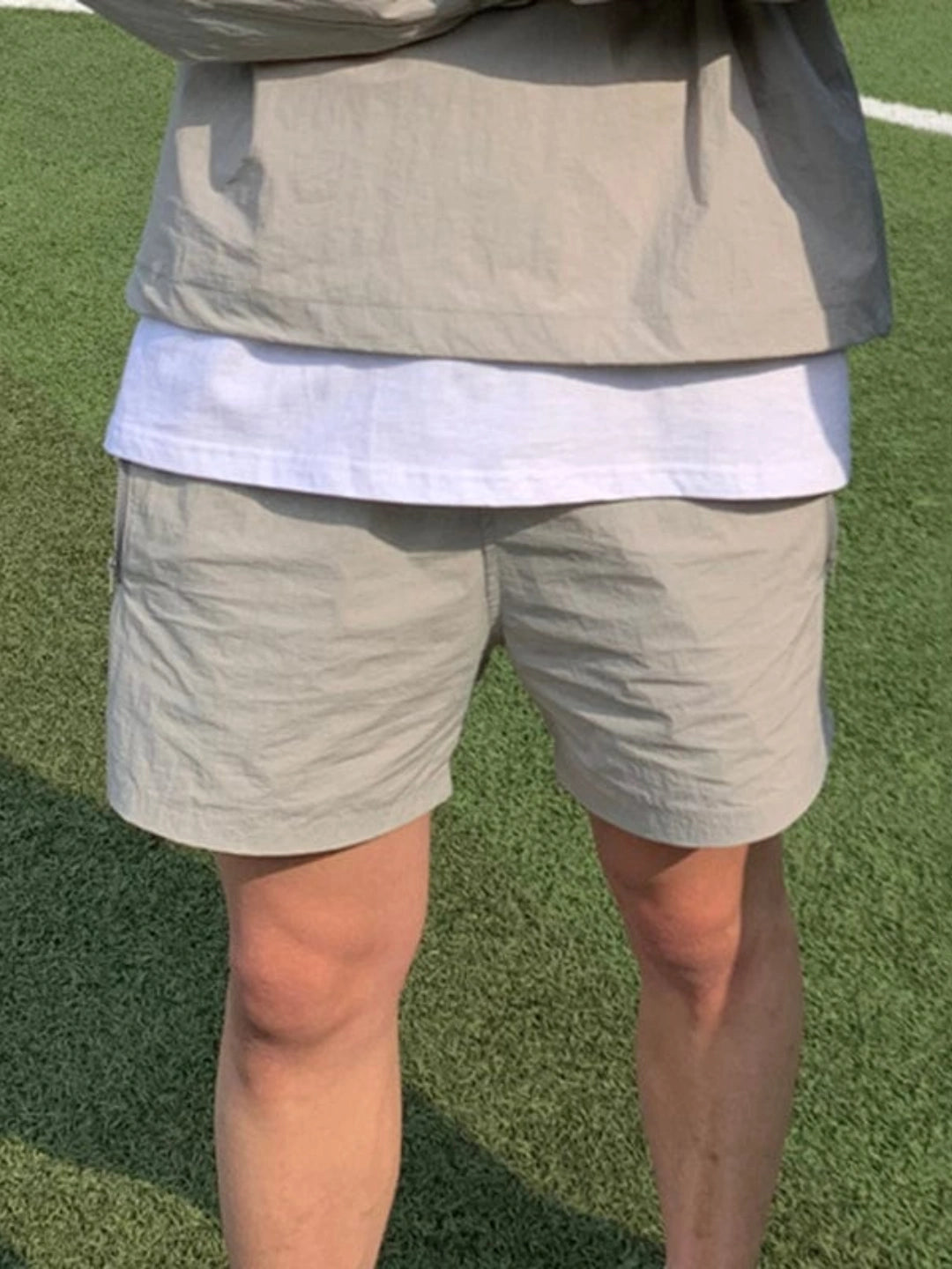 Person wearing light grey shorts and jacket on a white shirt on a grassy field