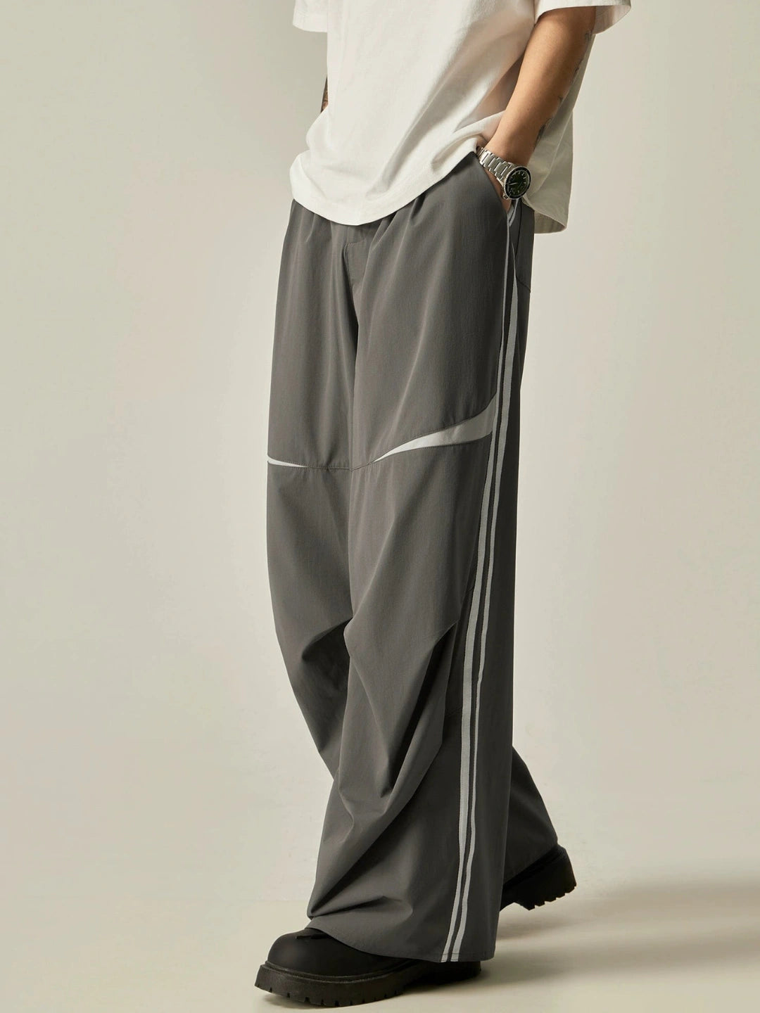 Person wearing grey wide-leg pants with a white stripe on a plain background