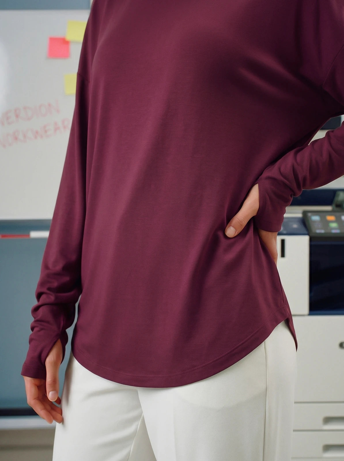 Person wearing a maroon long-sleeve shirt and white pants in an office setting