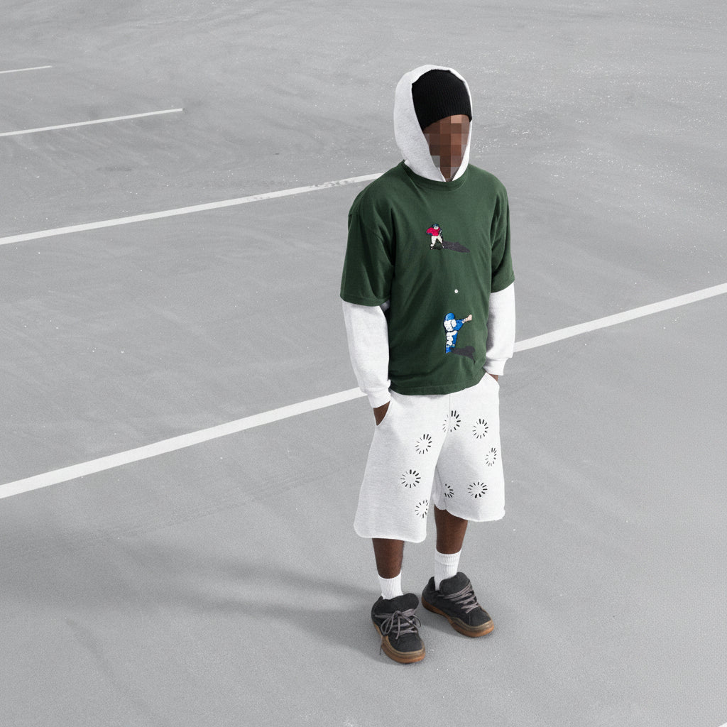 Person wearing a green hoodie and white pants on a grey tennis court