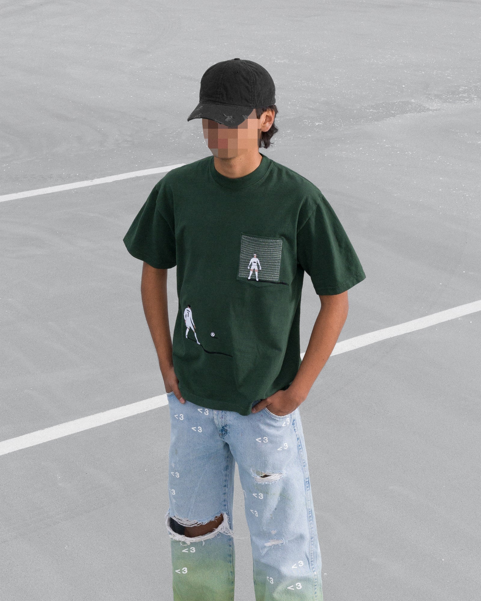 Person wearing a dark green t-shirt with a graphic design and light blue jeans on a grey surface.