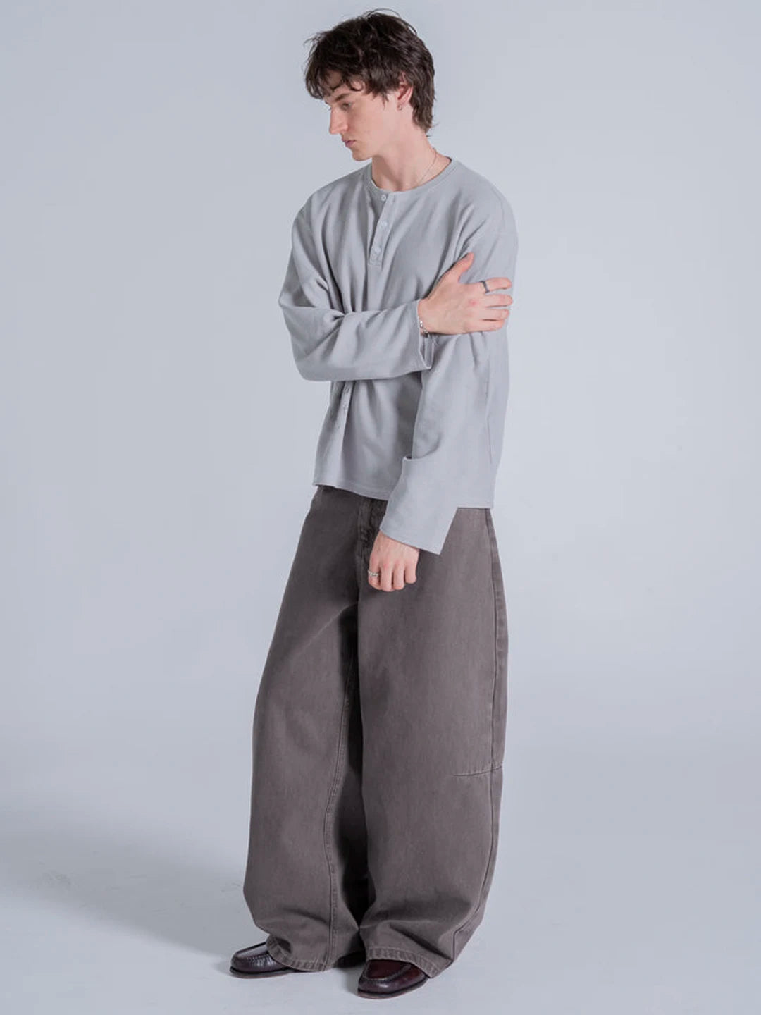 A man modeling a light grey long-sleeve henley t-shirt and wide-leg dark grey trousers 