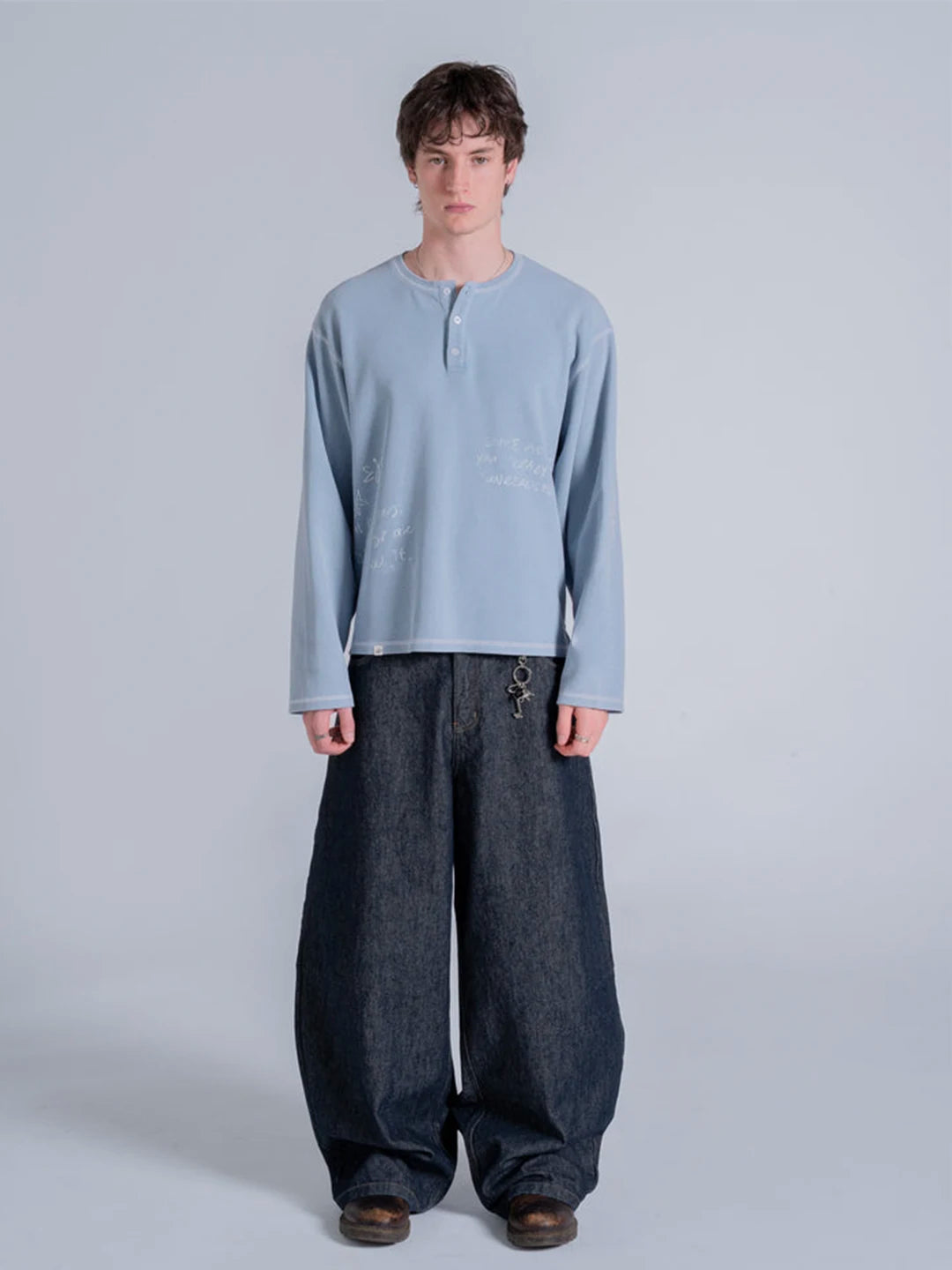 A model wearing a light blue long-sleeve henley t-shirt and very wide-leg dark blue jeans.