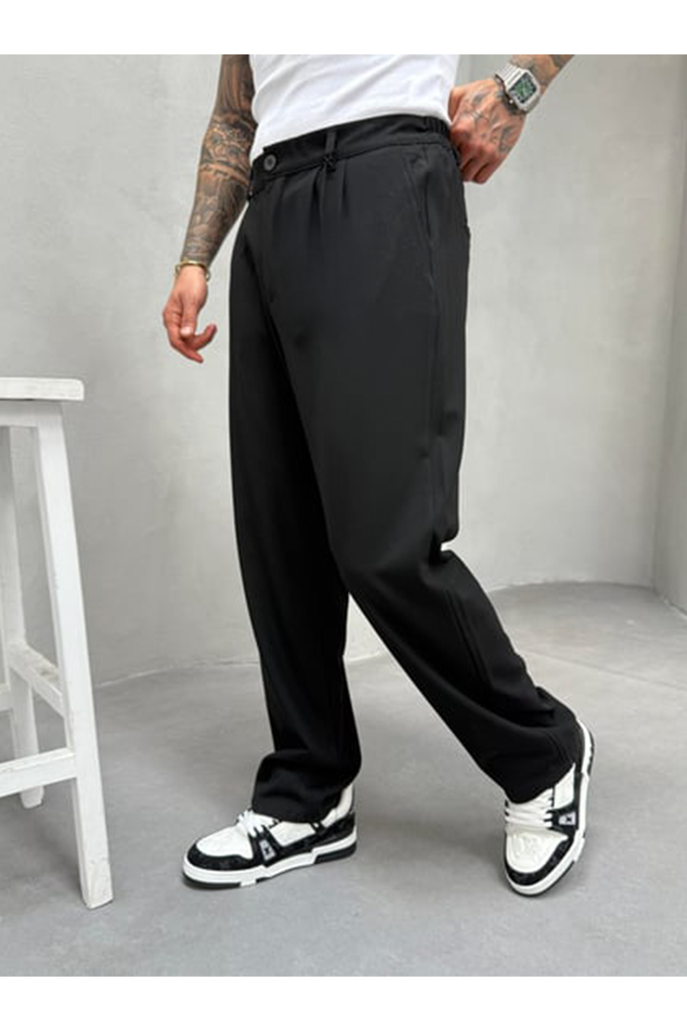 A person wearing black pants and white sneakers in a minimalistic setting