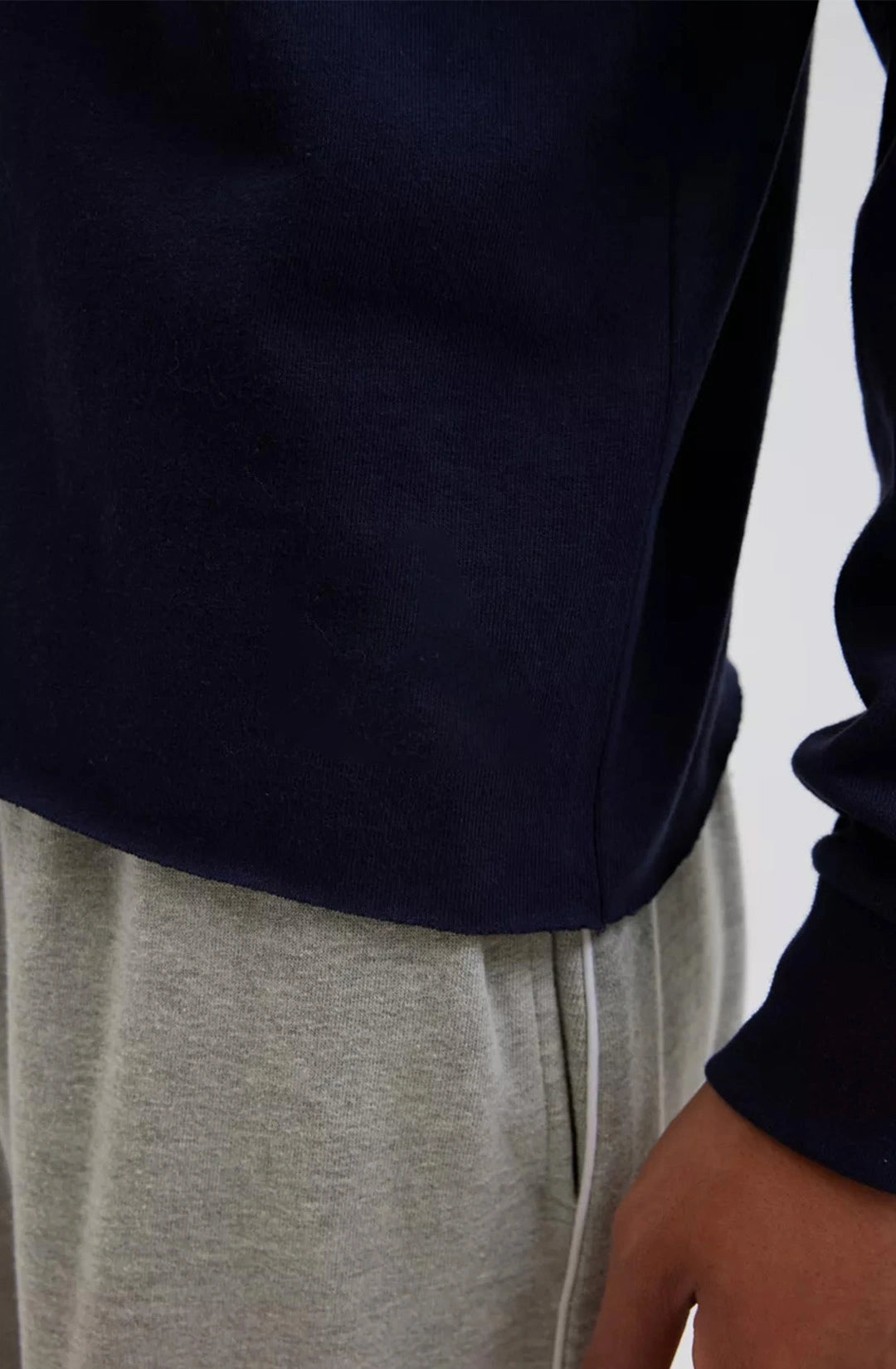 Person wearing a navy sweater and gray pants against a neutral background