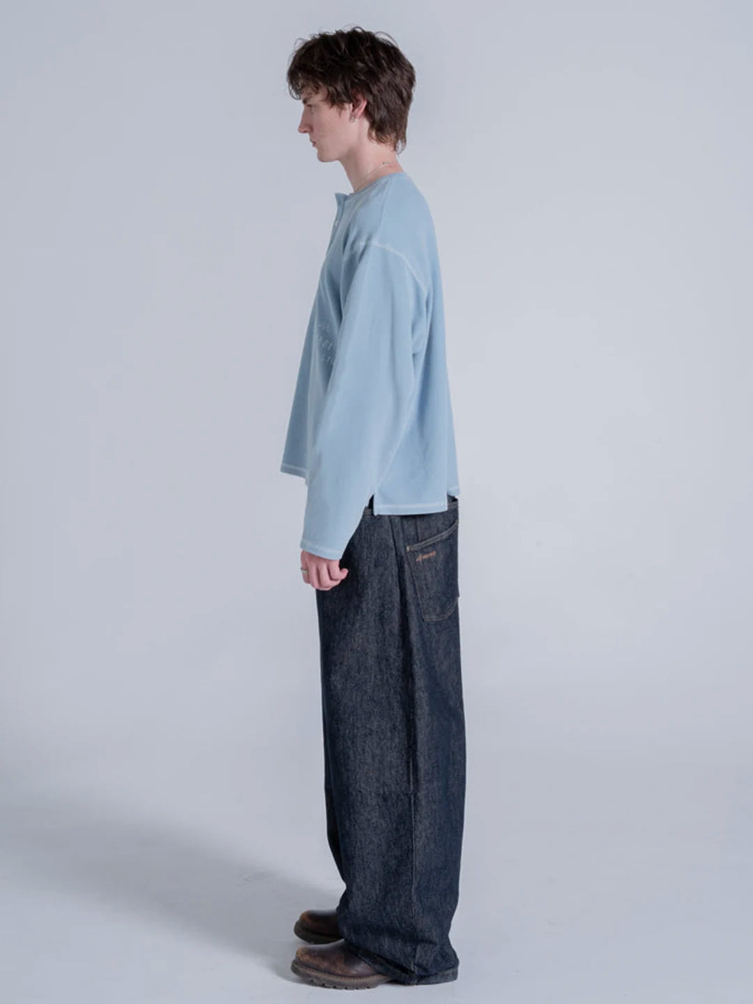 A model shown in profile wearing a light blue long-sleeve crewneck tshirt and dark wide-leg jeans 