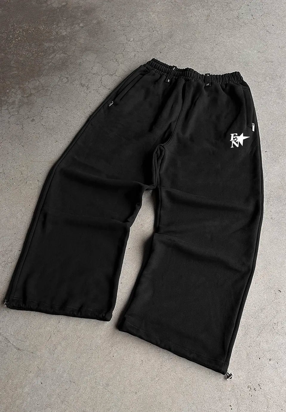 Black wide-leg sweatpants with an elastic waistband and a white graphic logo on the upper left thigh