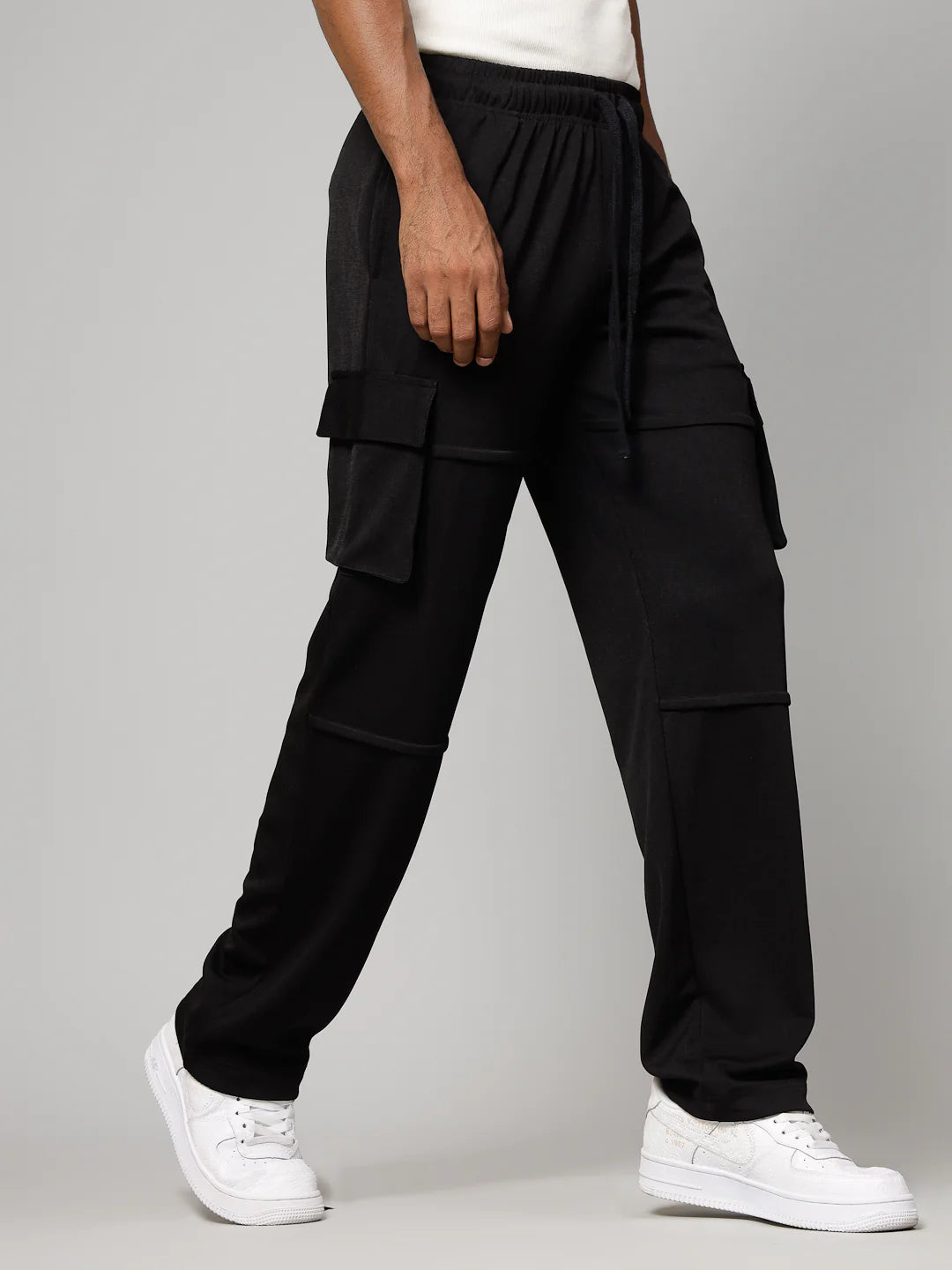 Person wearing black cargo pants and white sneakers on a grey background