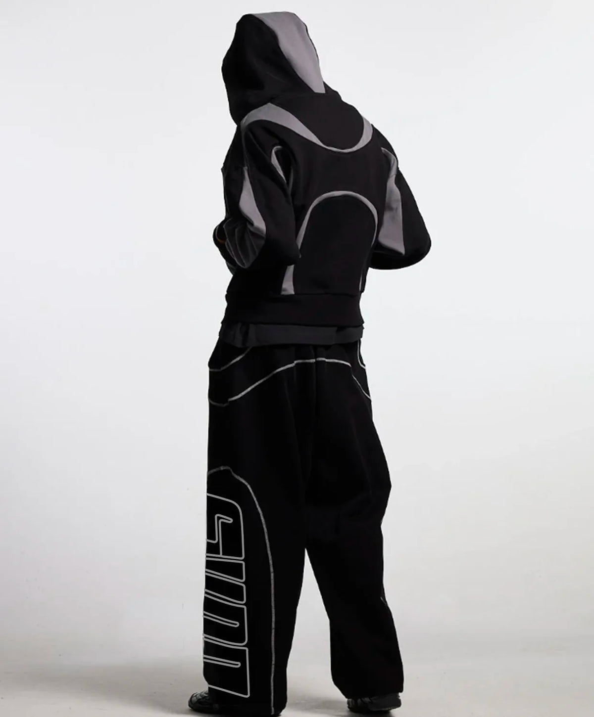 A person wearing a black hooded jacket and matching black pants with grey and white graphic details