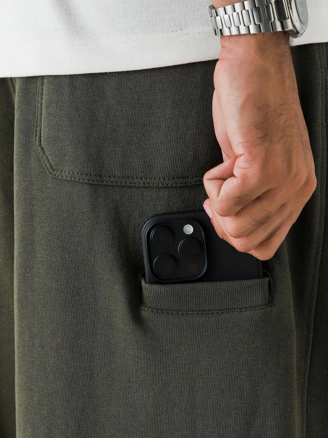 Person putting a smartphone into a pocket of dark pants with a white shirt and silver watch.