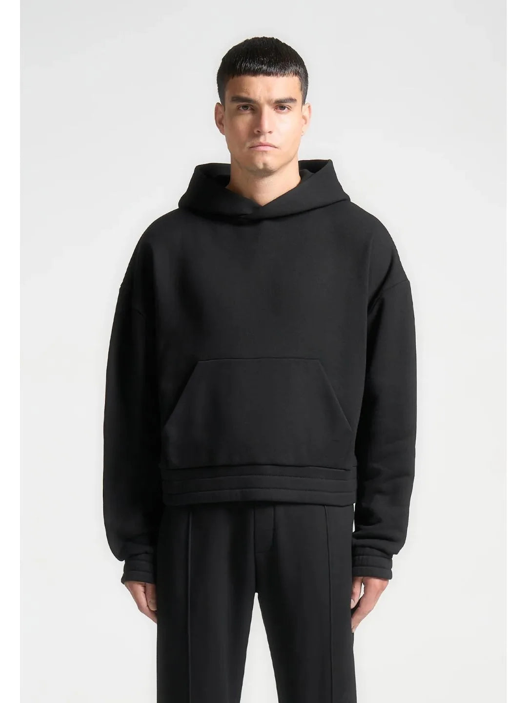 Person wearing a black hoodie and pants on a white background