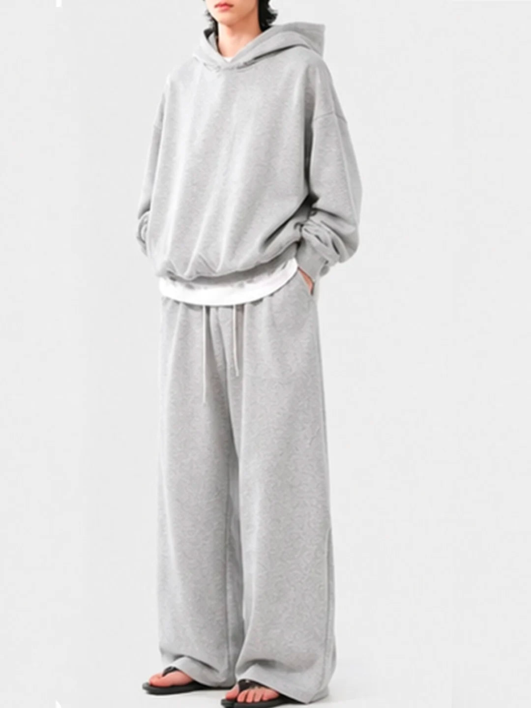 Person wearing a grey hoodie and wide-leg pants on a white background