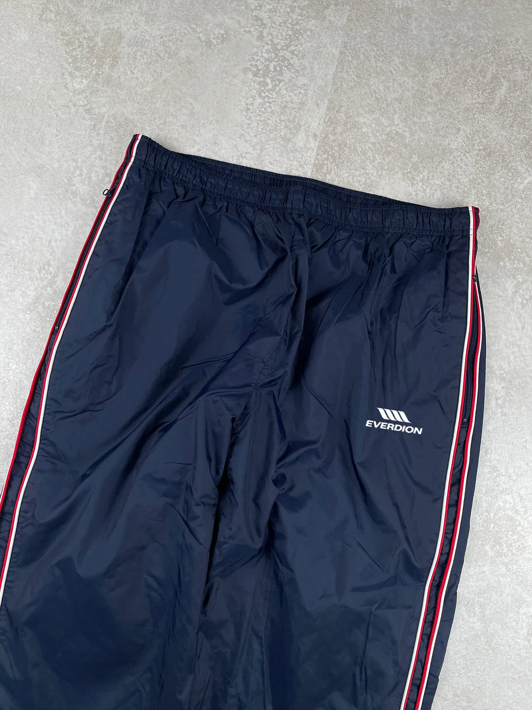 Navy track pants with a red stripe and brand logo on a grey background