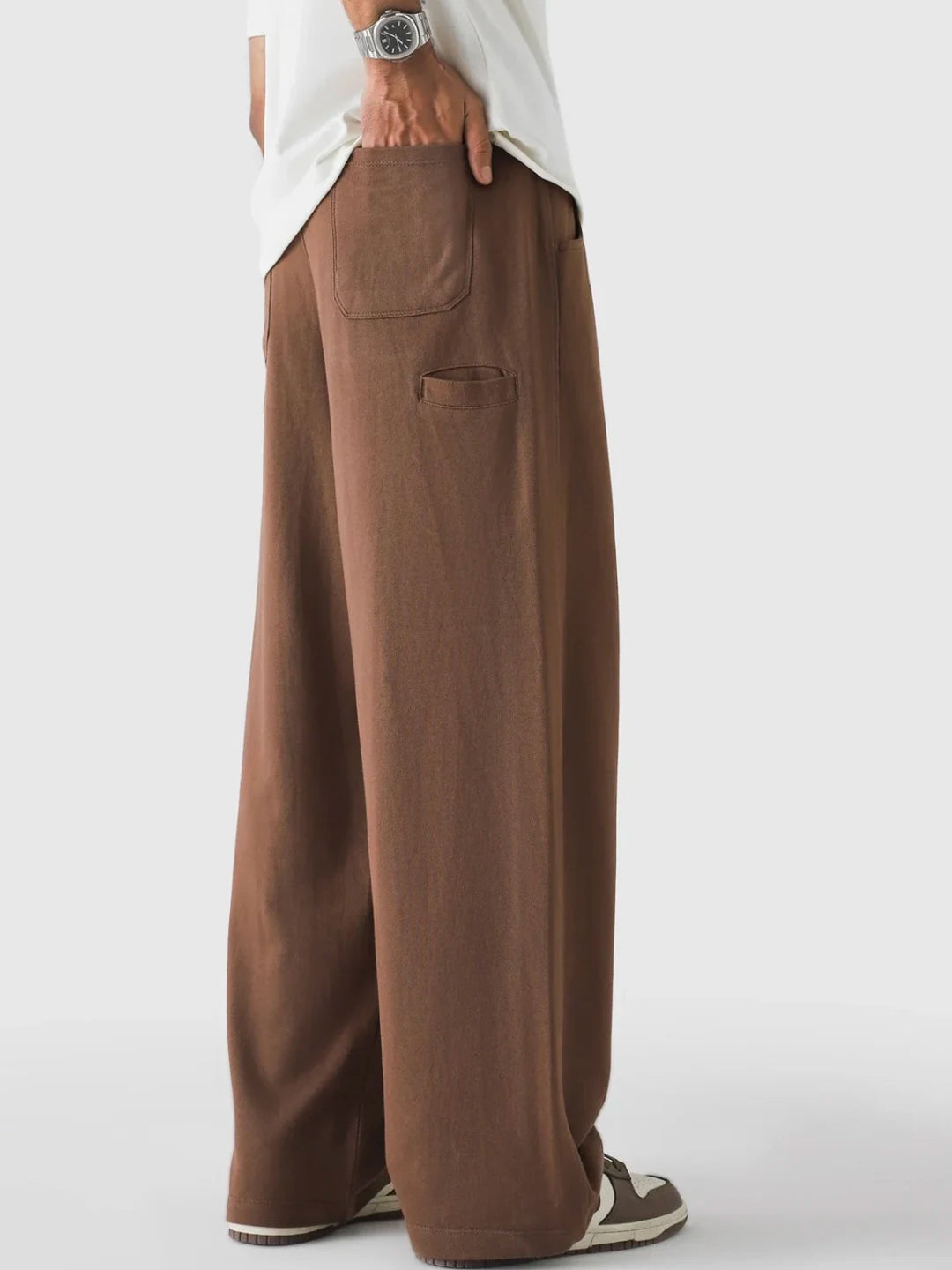 Brown wide-leg pants worn with a white shirt on a light grey background