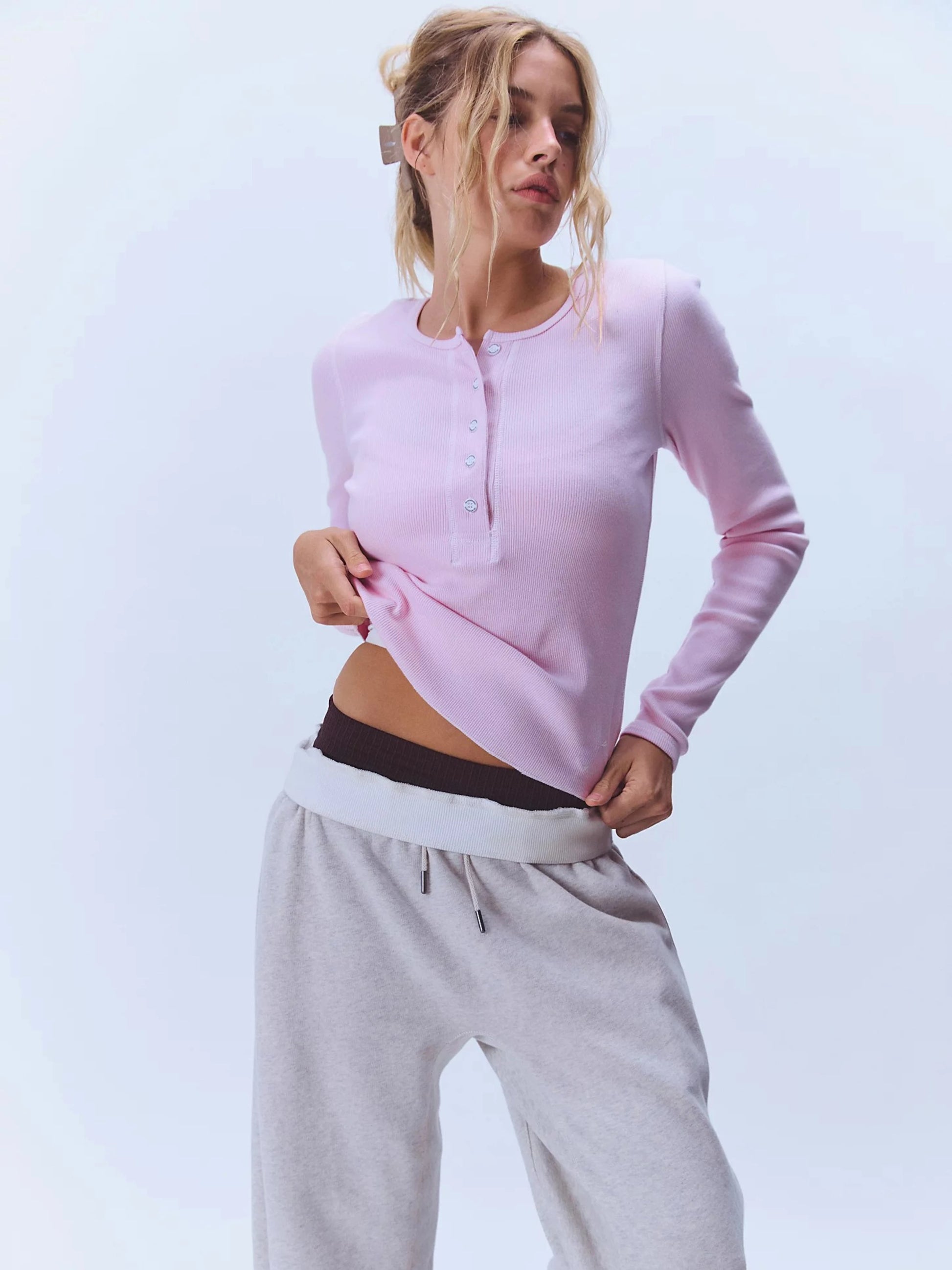 Woman wearing a pink long-sleeve top and gray sweatpants on a light blue background