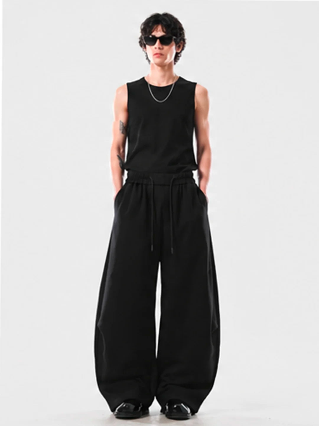 Person wearing a black sleeveless top and wide-leg pants on a white background