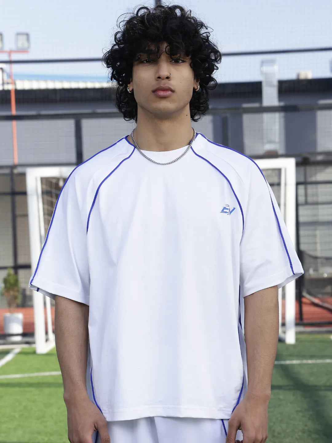 Person wearing a white sports t-shirt with blue accents on a sports field.