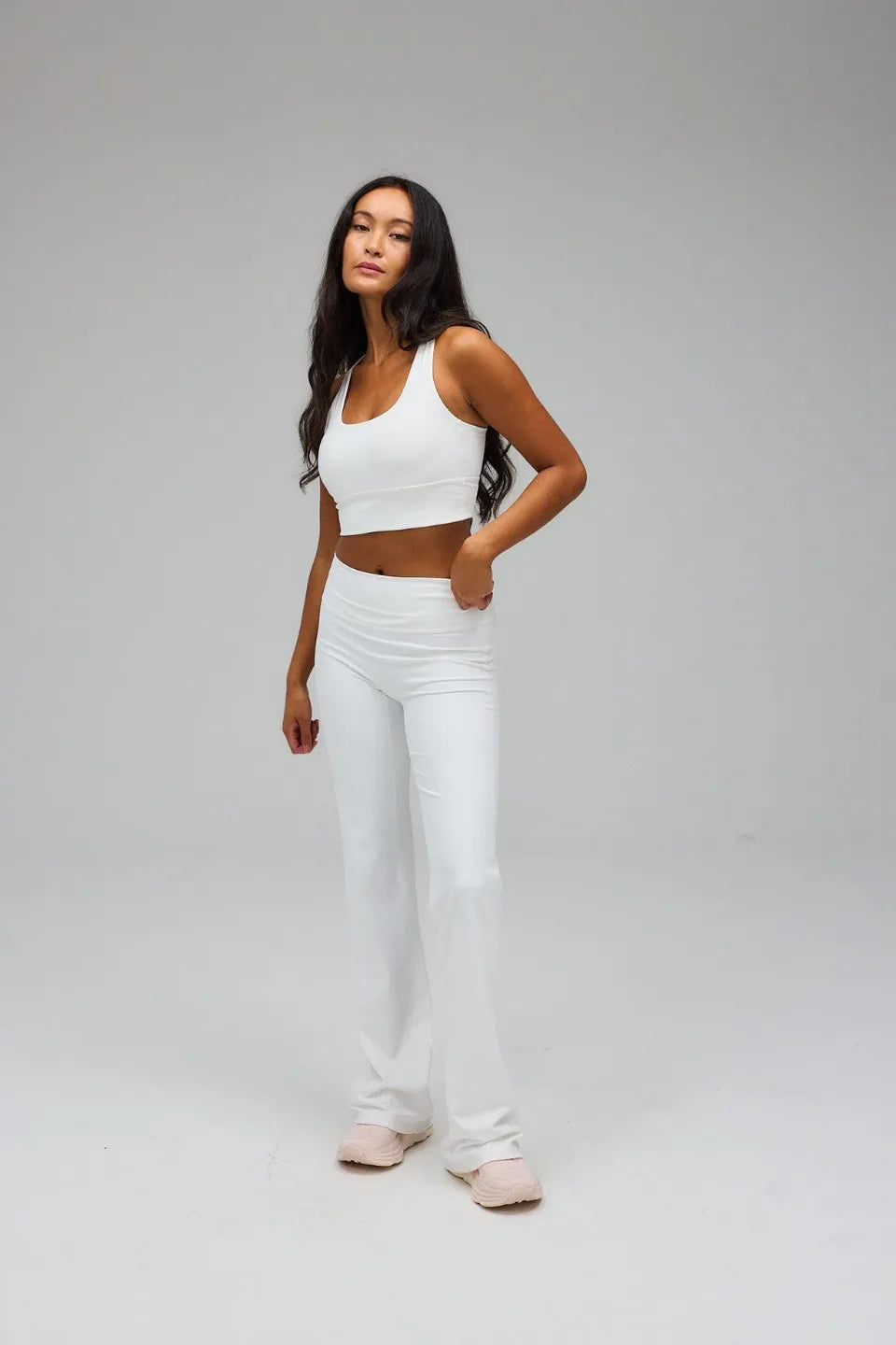 Woman wearing a white sports bra and pants on a grey background