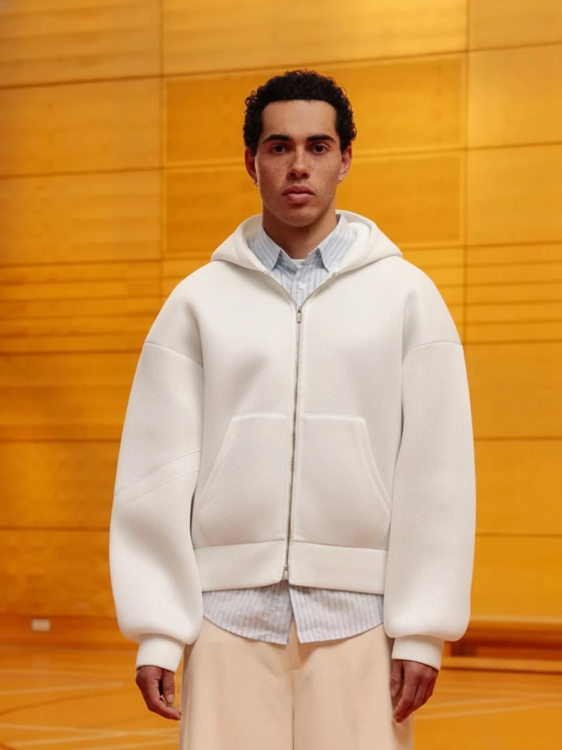 Man wearing a white hoodie over a patterned shirt with a wooden background