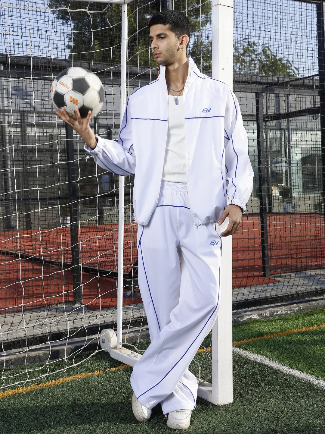 Person in a white sports tracksuit holding a soccer ball on a sports field.