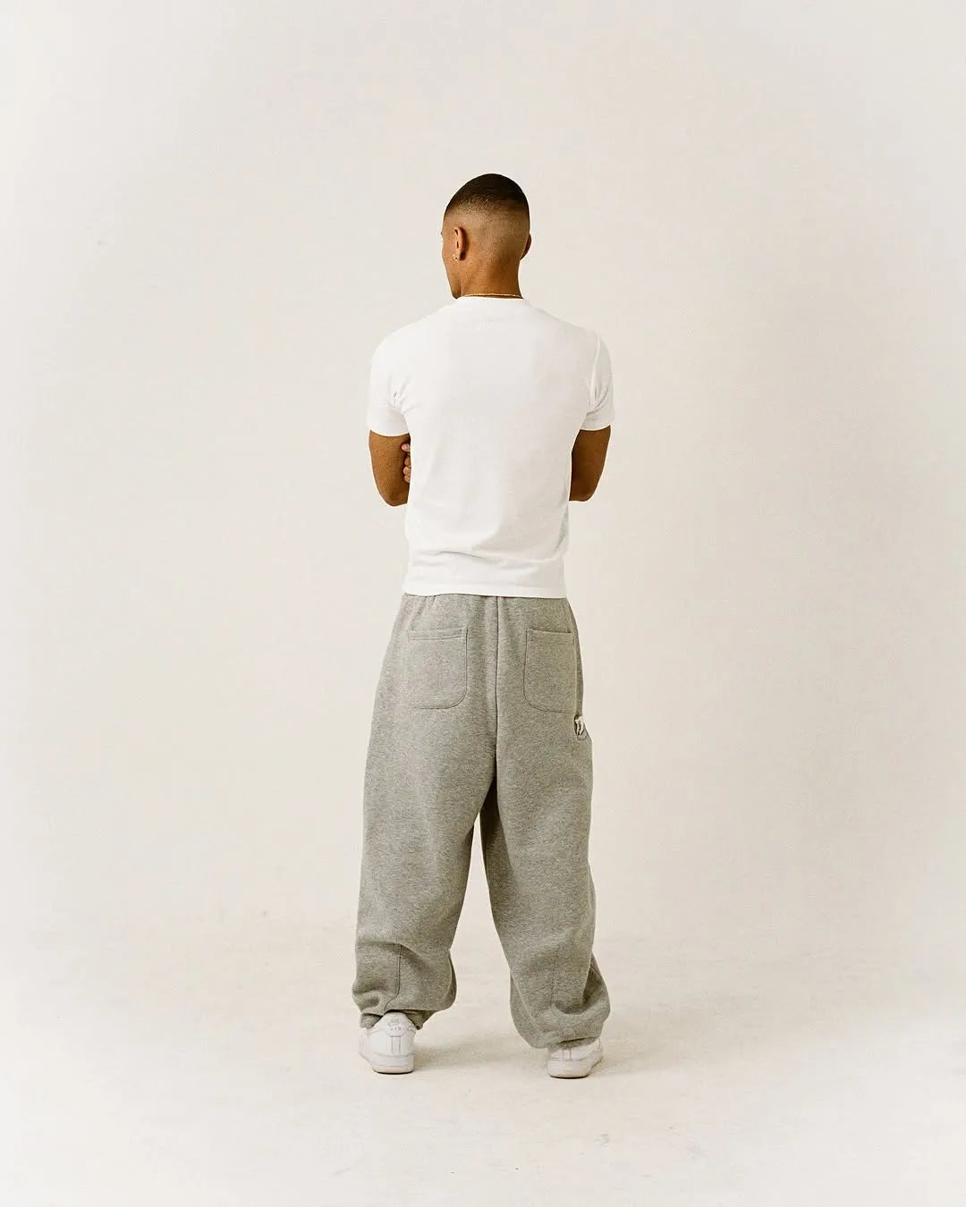 Person wearing a white fitted t-shirt and grey sweatpants on a plain background