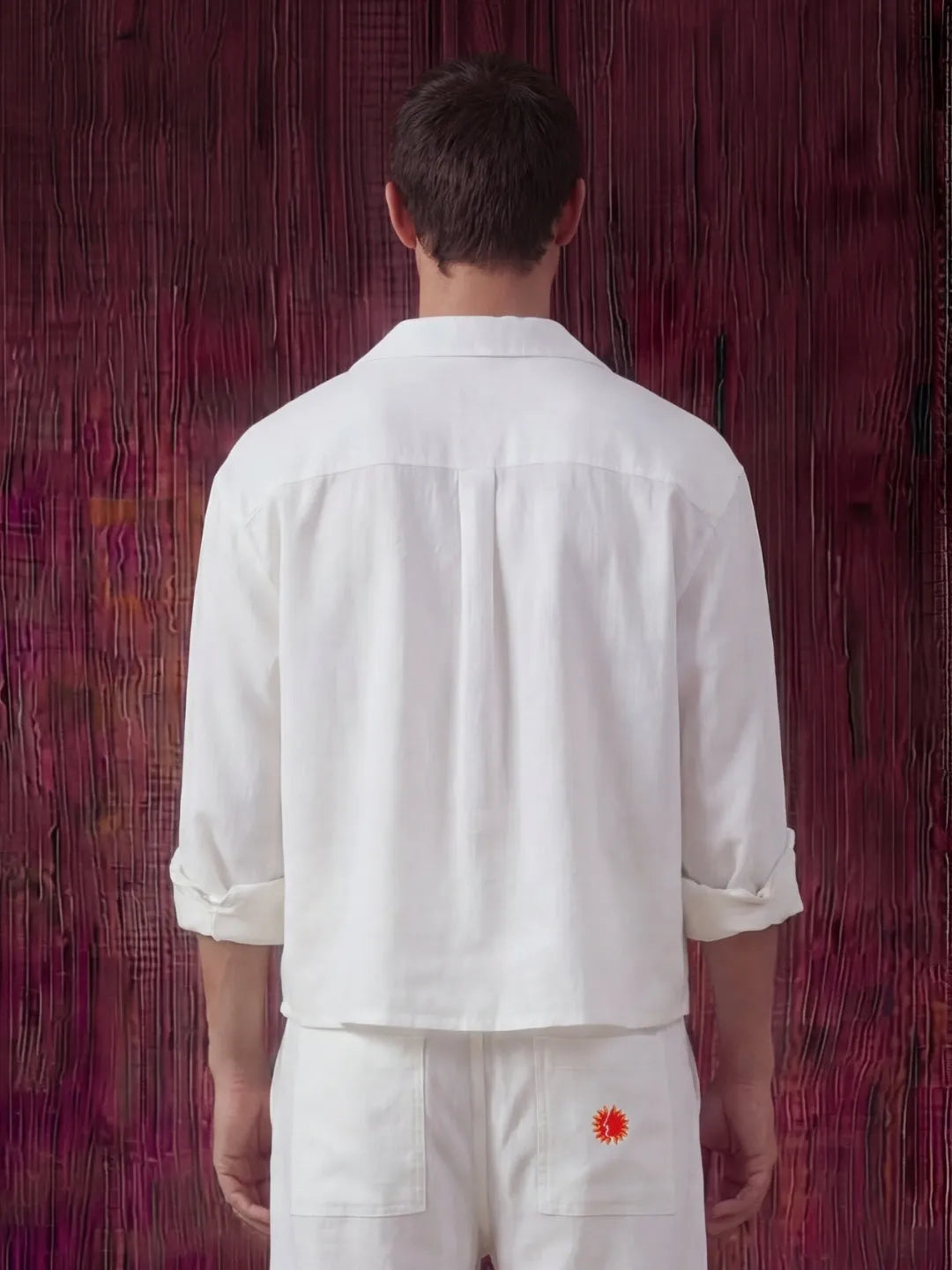 Person wearing a white shirt and pants with a red flower design against a textured purple wall.