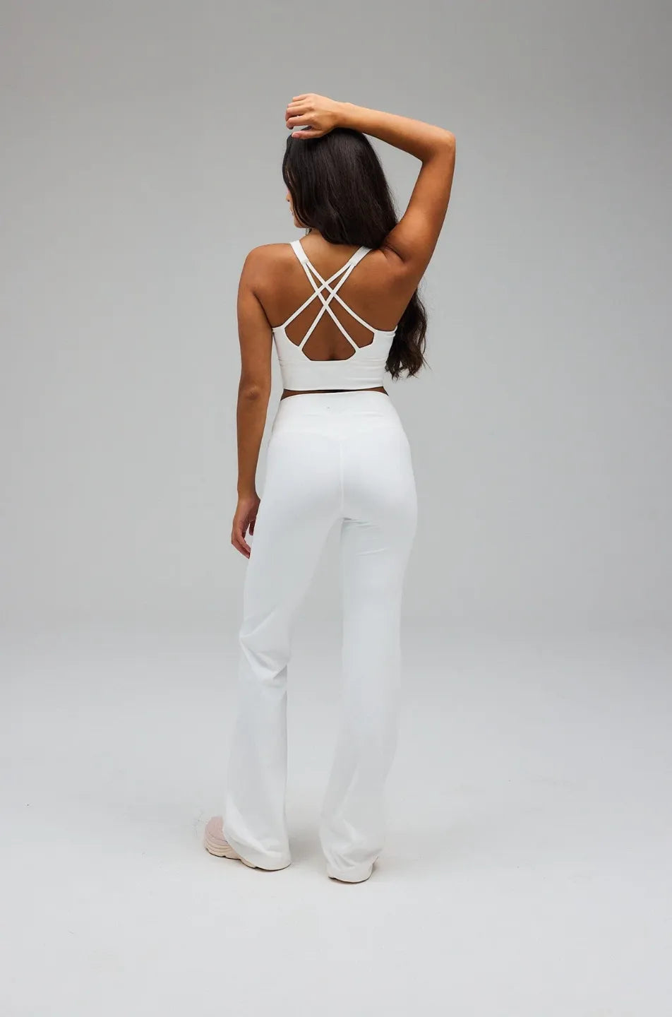 Person wearing a white outfit with criss-cross straps on a grey background