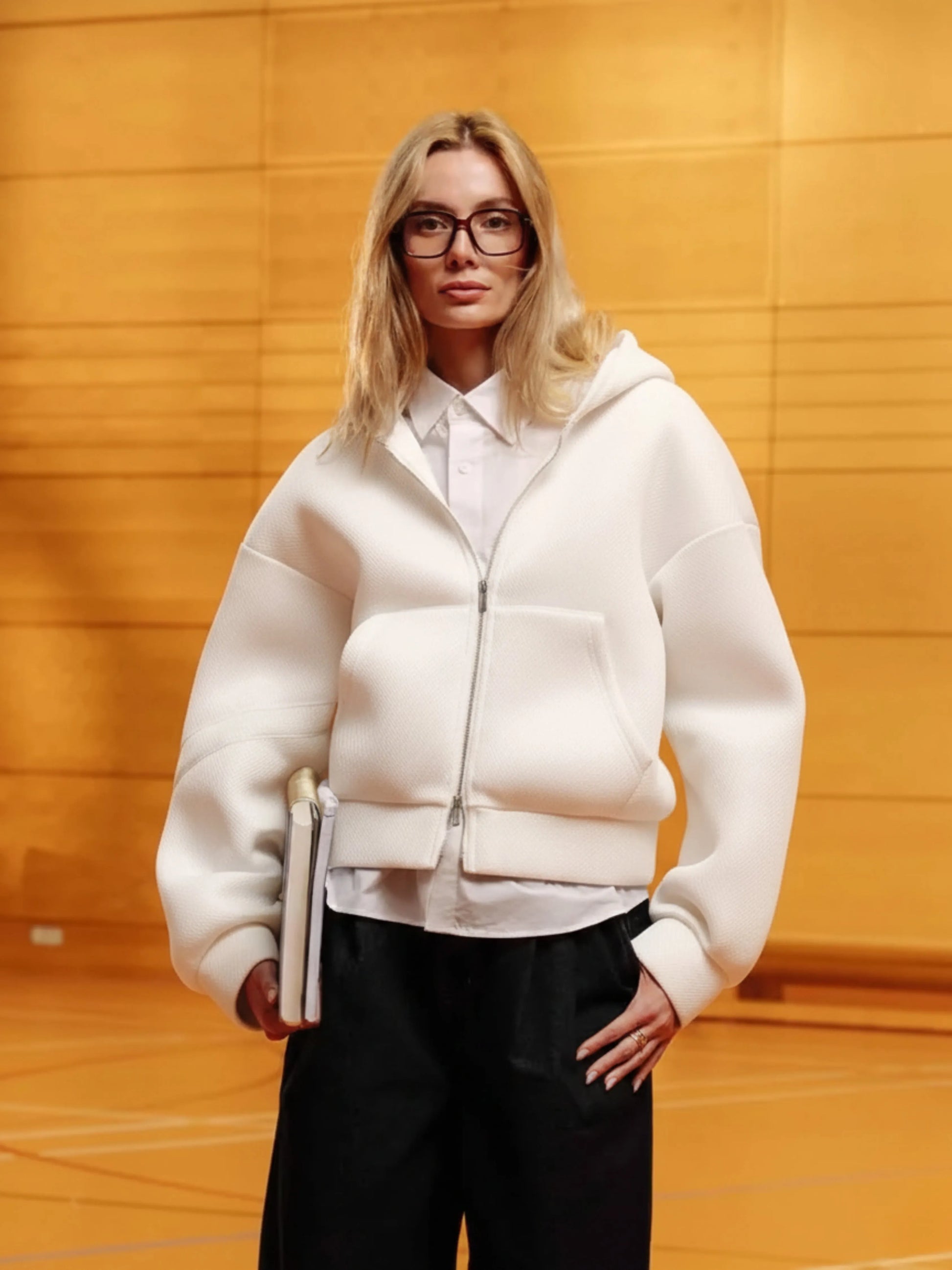 Person wearing a white hoodie and black pants against a yellow wall