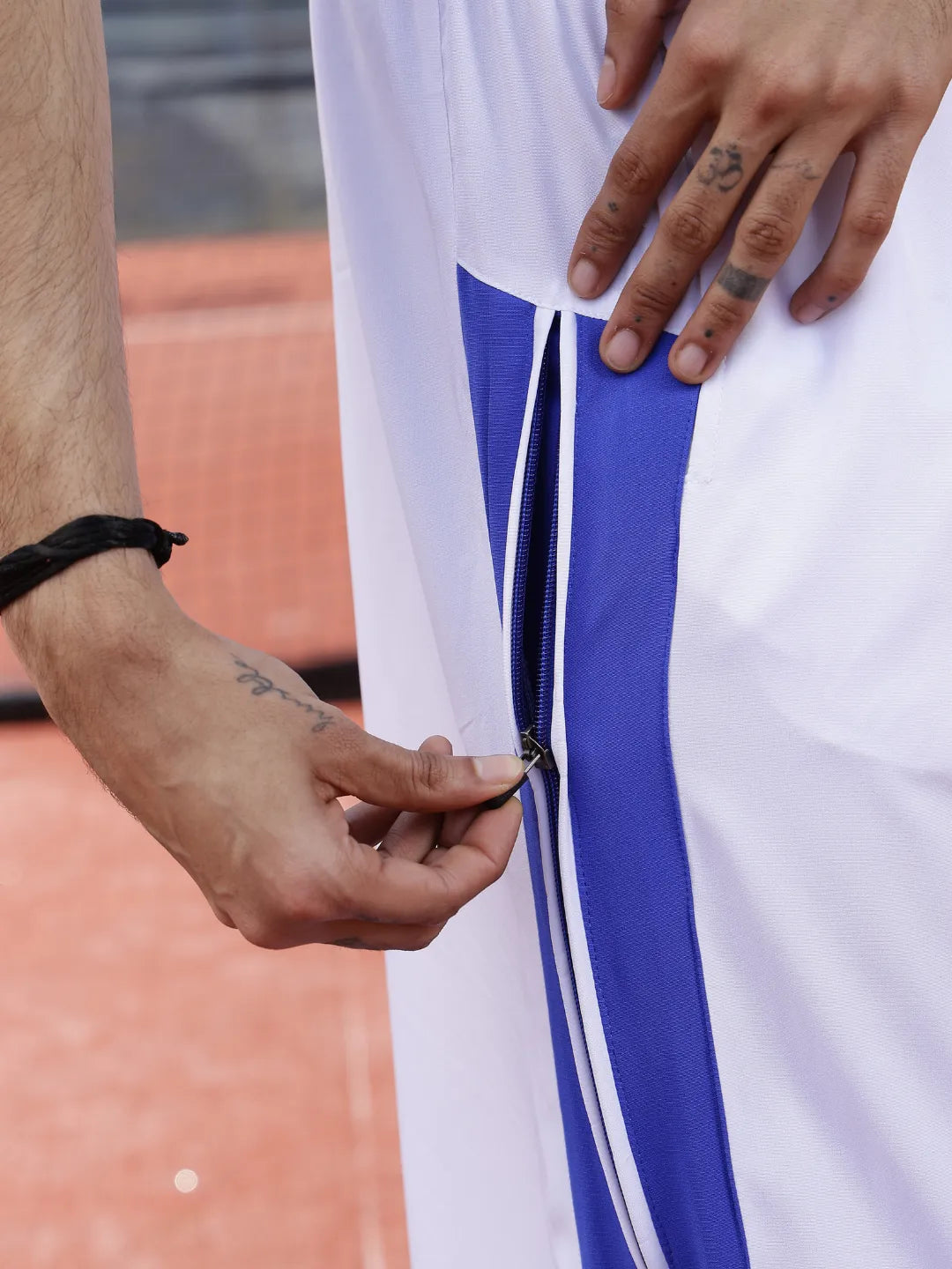 Person wearing white sports pants with blue stripes and 'Everdion' branding on a tennis court.