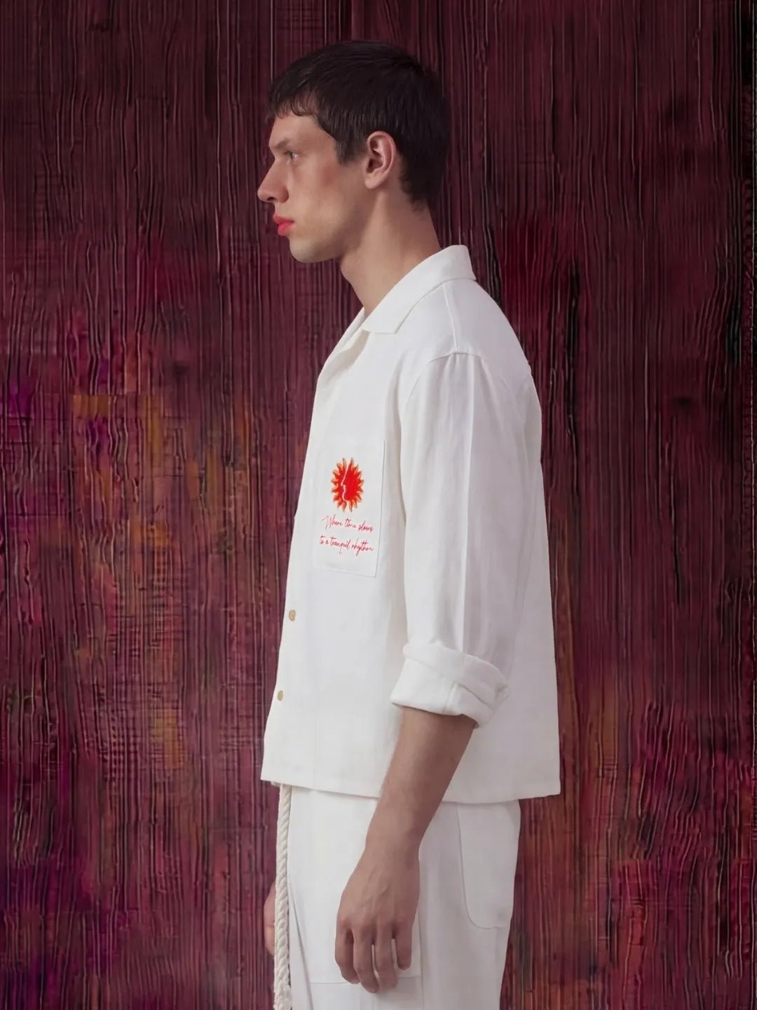 Person wearing a white outfit with a red emblem against a textured red background
