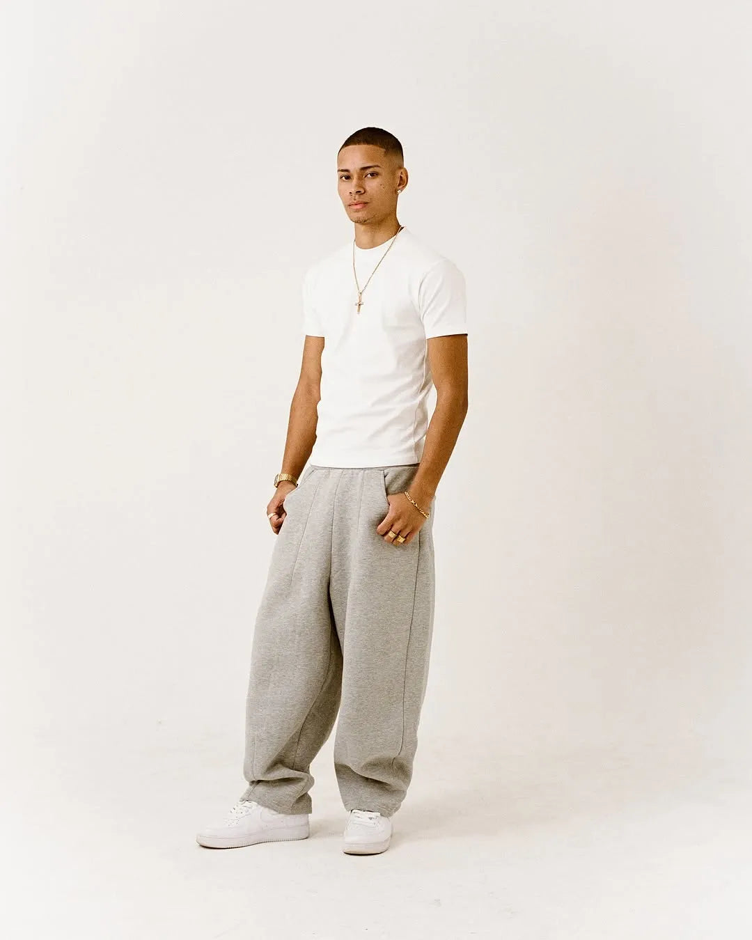 Person wearing a white fitted t-shirt and grey sweatpants on a plain background