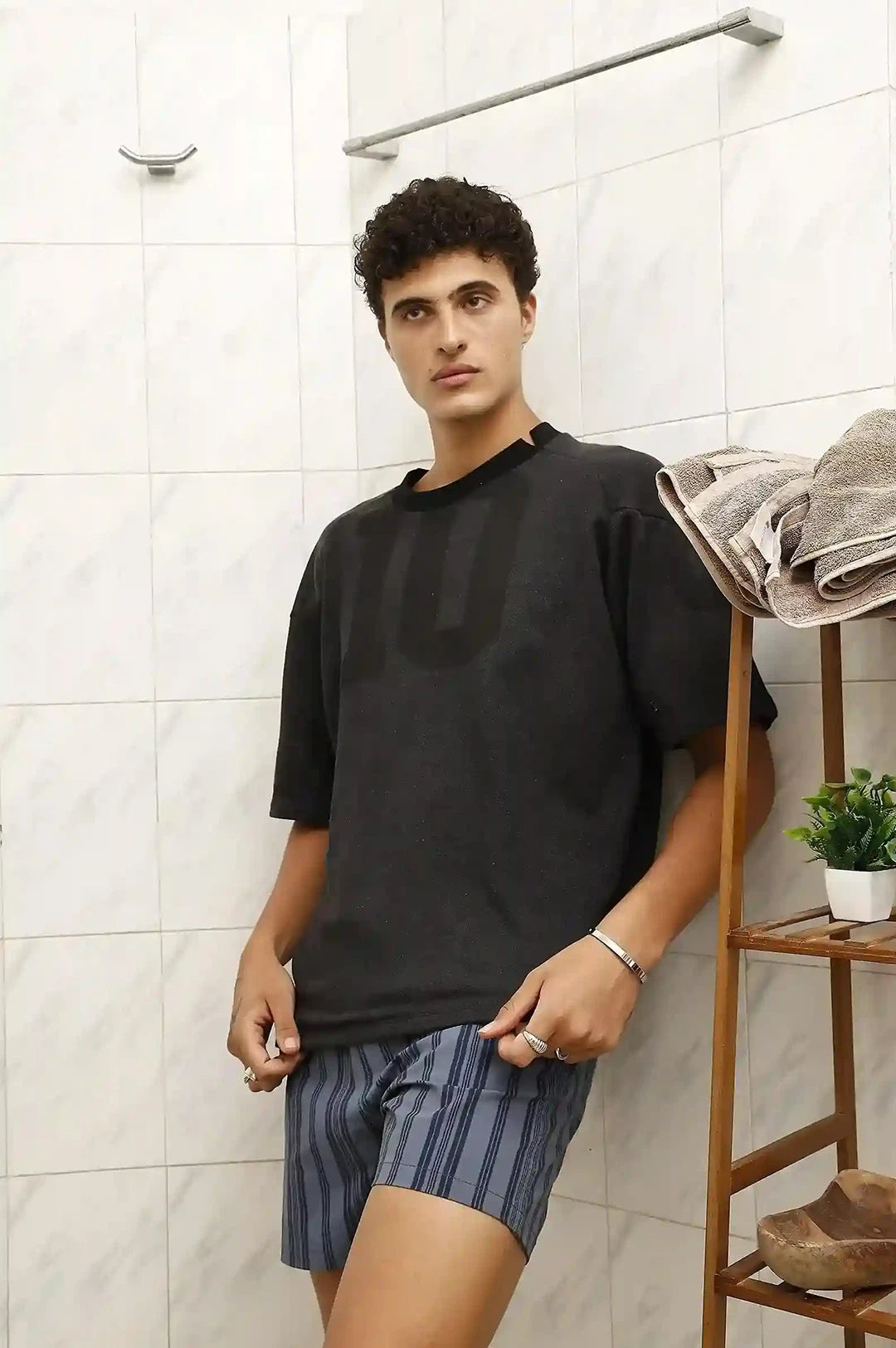 Man wearing a black t-shirt and striped shorts in a bathroom.