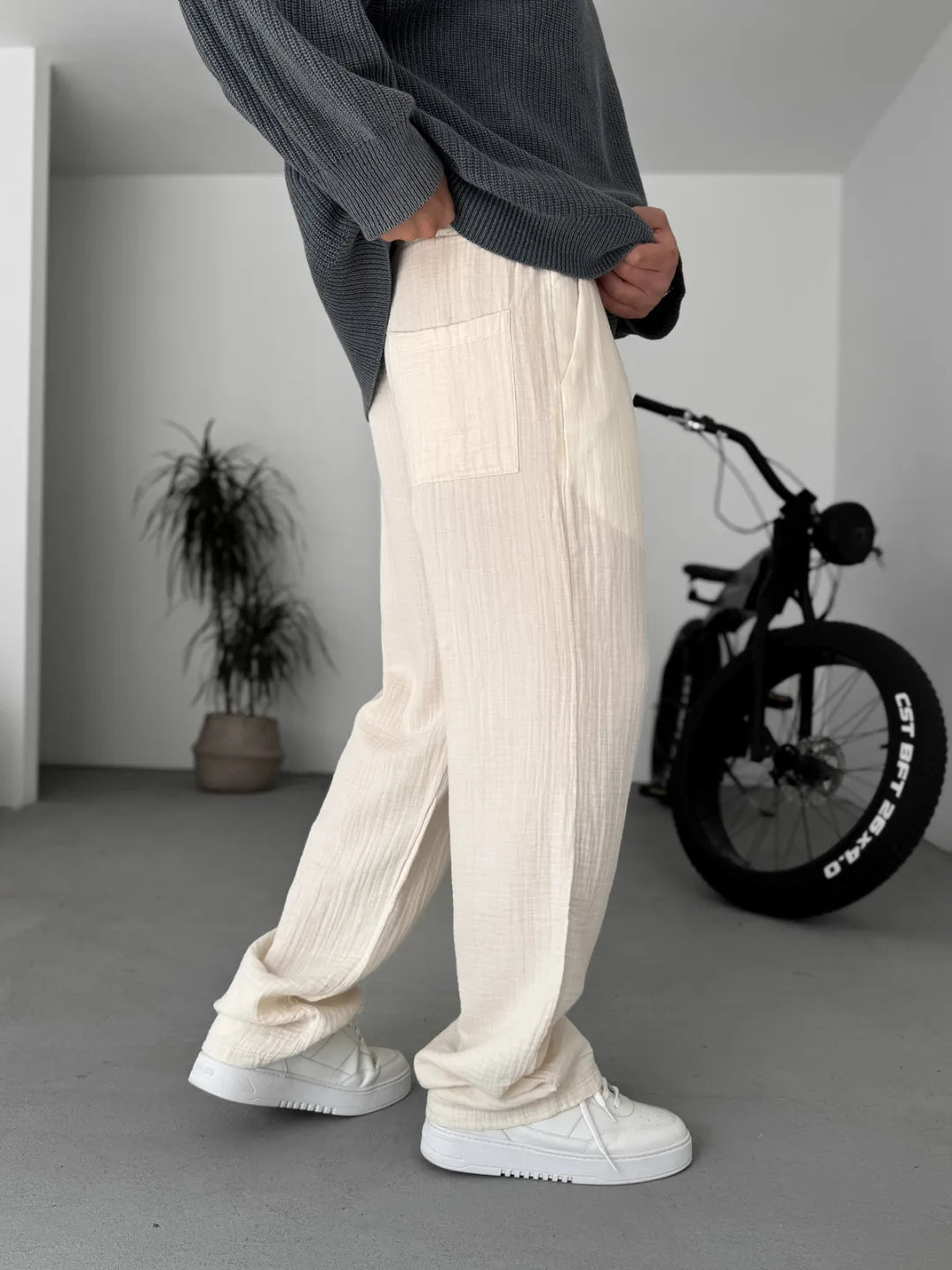 Person wearing cream ribbed pants and white sneakers in a minimalistic room with a bicycle in the background.