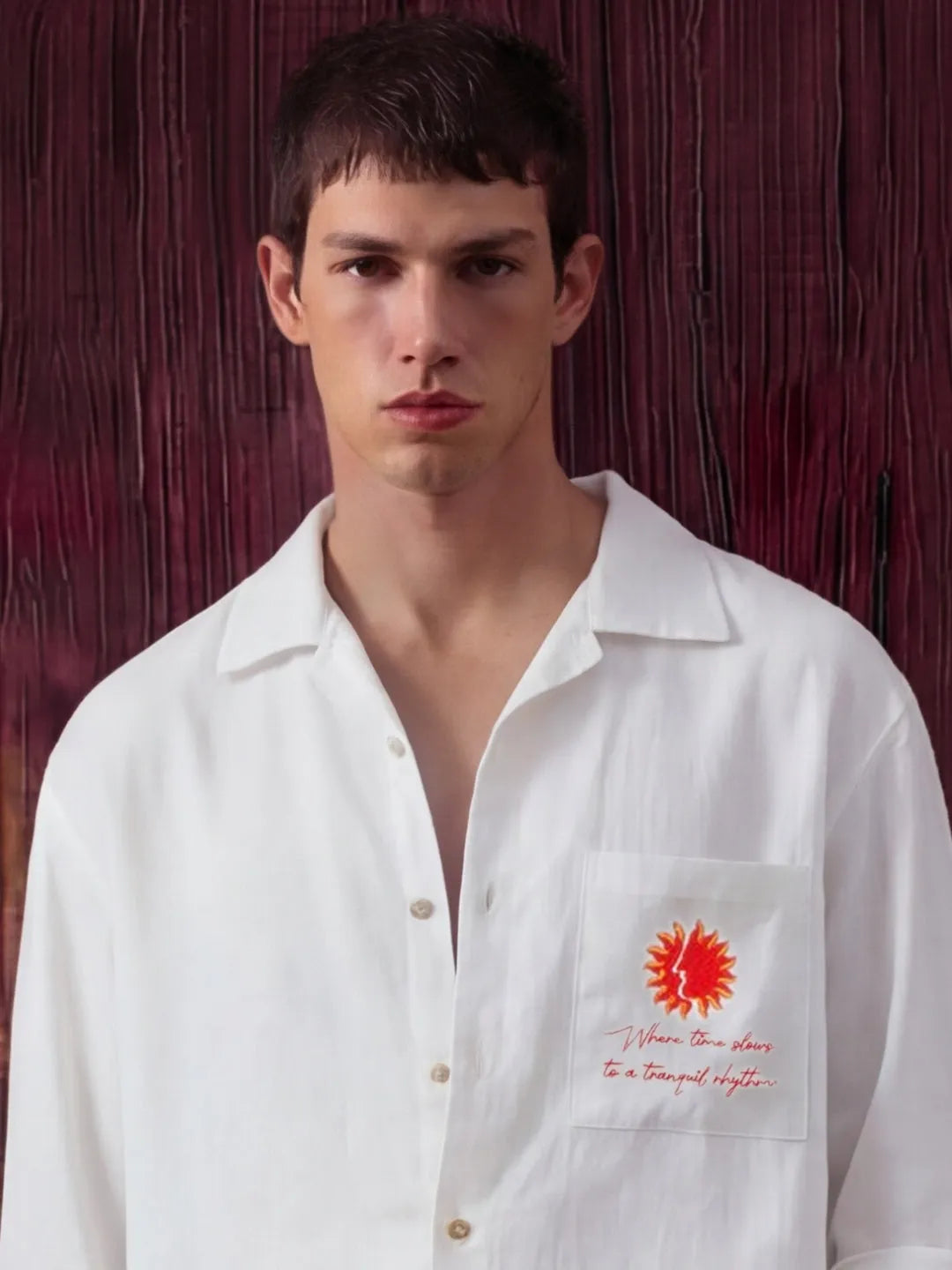 Man wearing a white shirt with a red sun design and text against a dark background