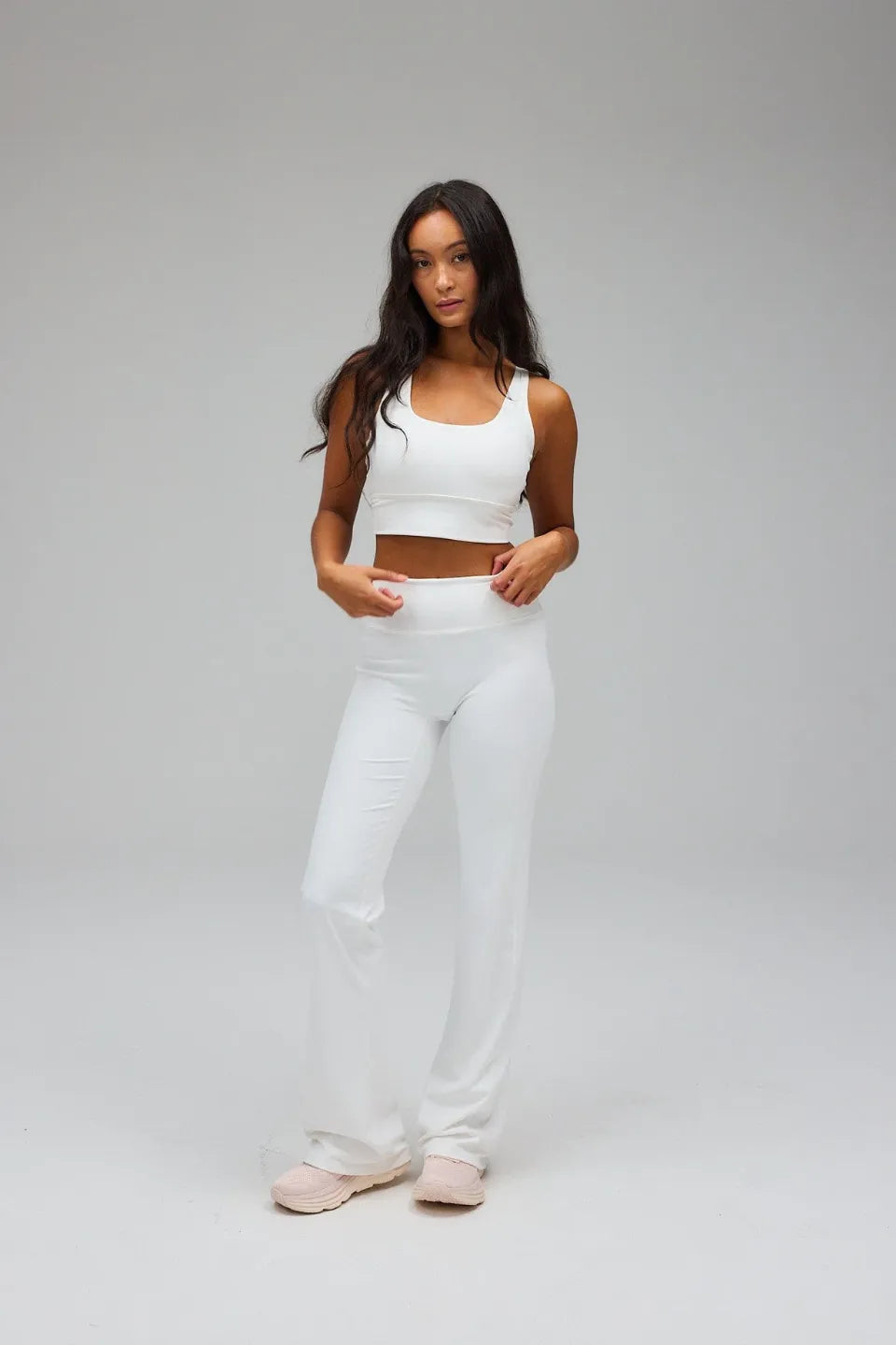 Woman wearing a white sports bra and pants on a grey background
